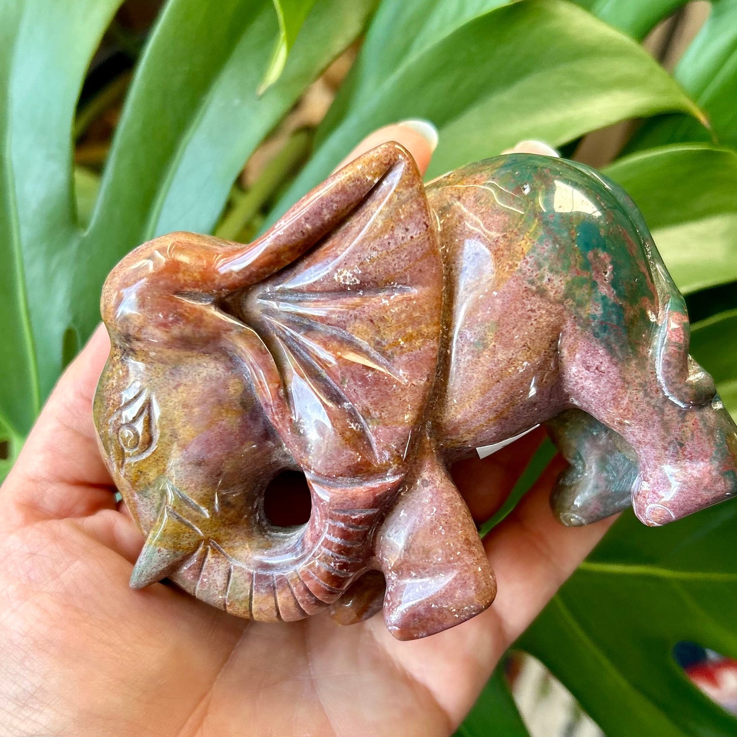 Hand holding a stone sculpture of a creature against a green leafy background