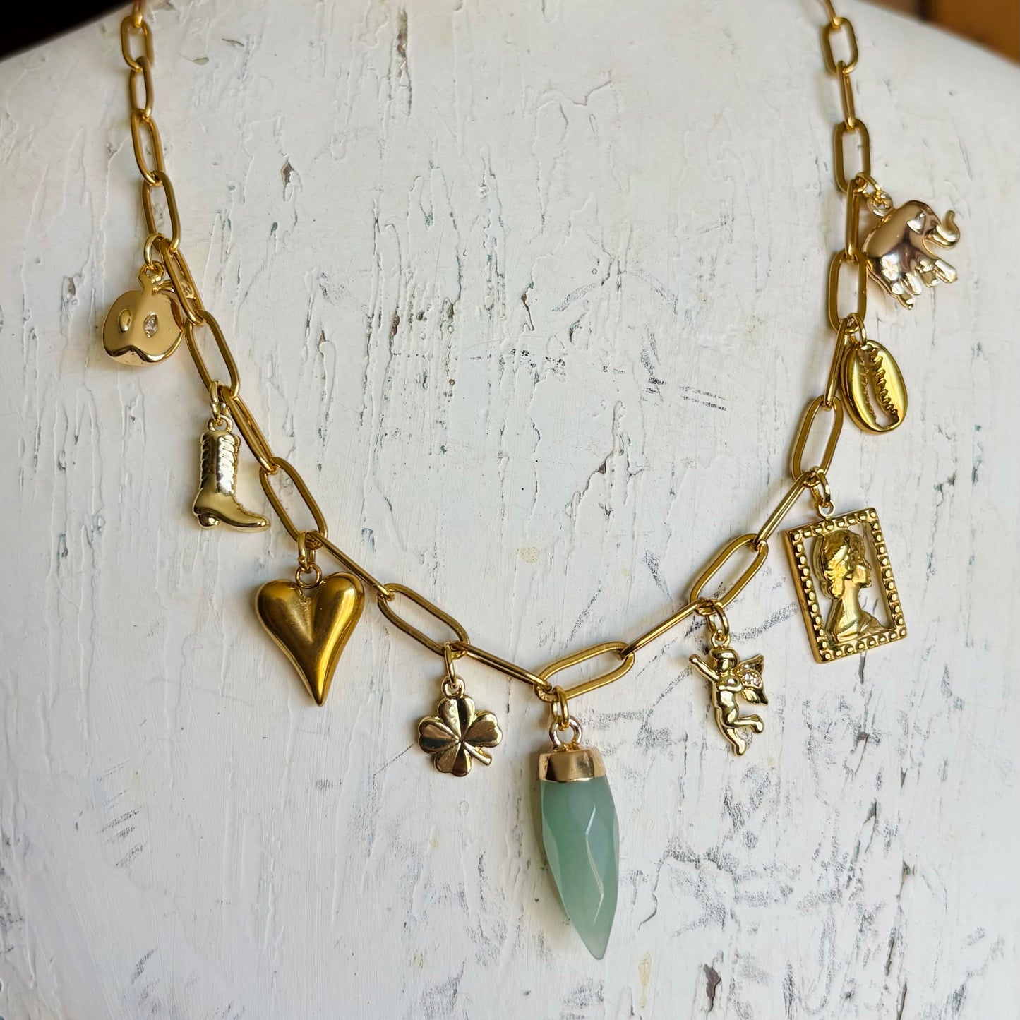 Gold necklace with various charms on a mannequin bust.