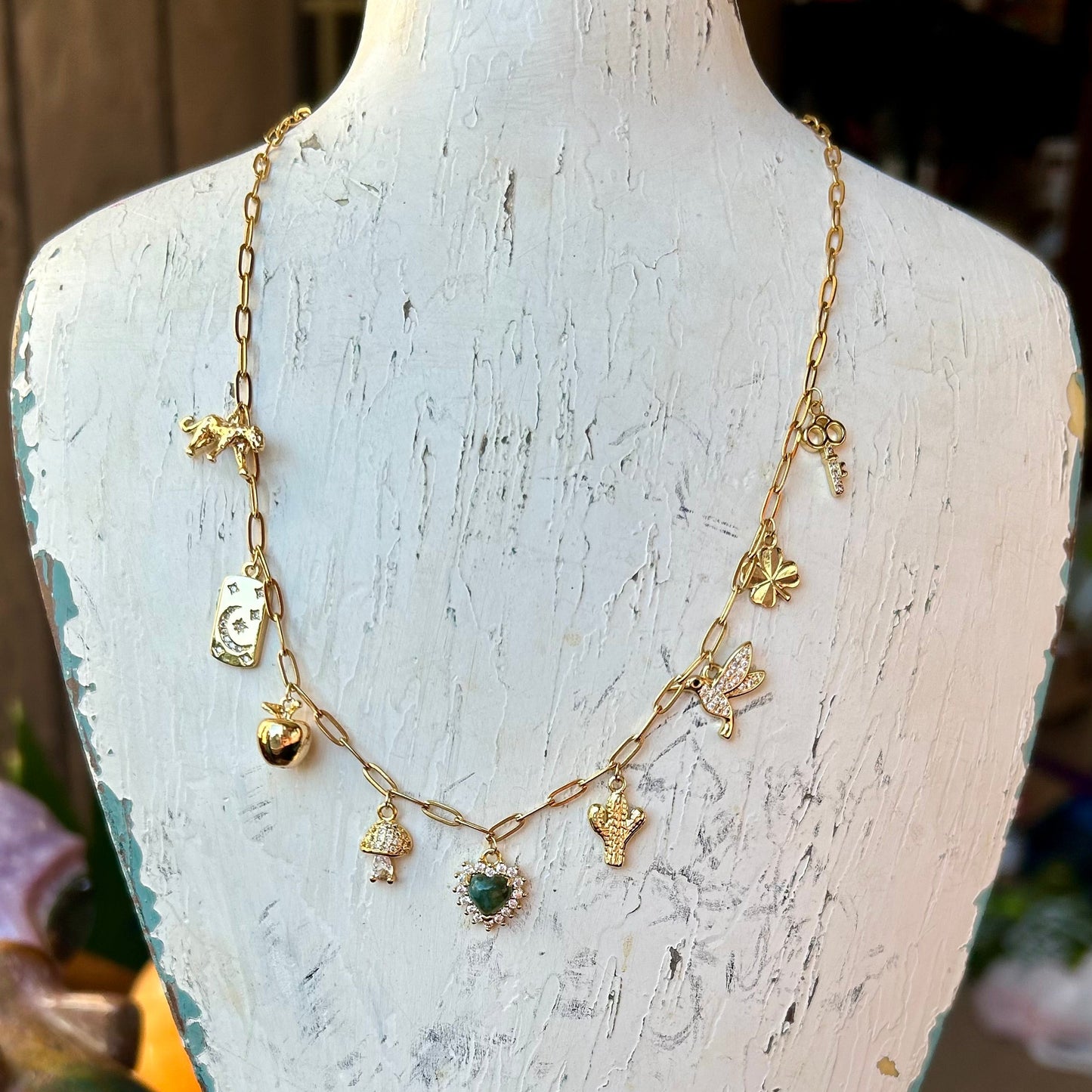 Gold necklace with charms on a white distressed wooden stand.