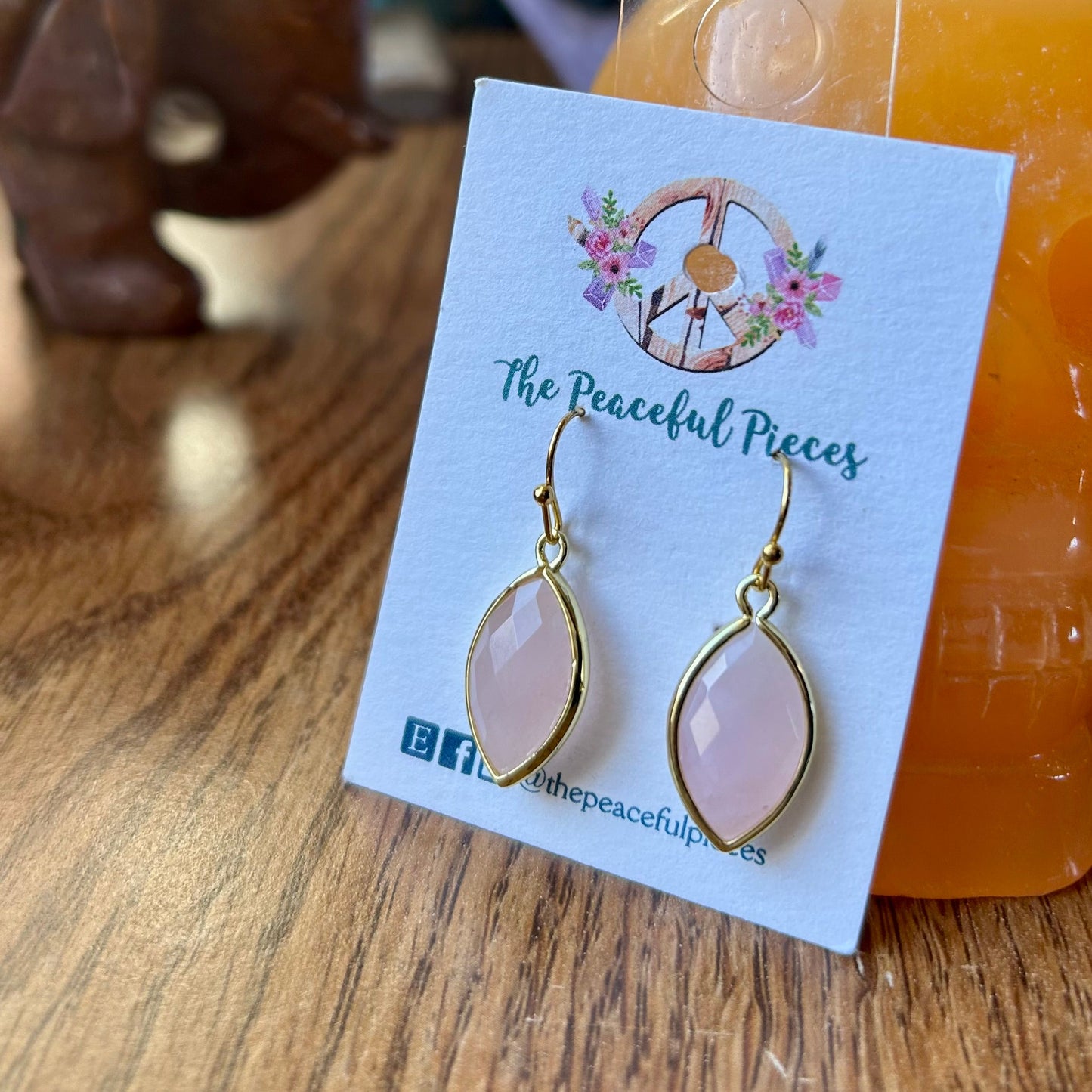 Teardrop-shaped earrings on a card with 'The Peaceful Pieces' branding, displayed on a wooden surface.