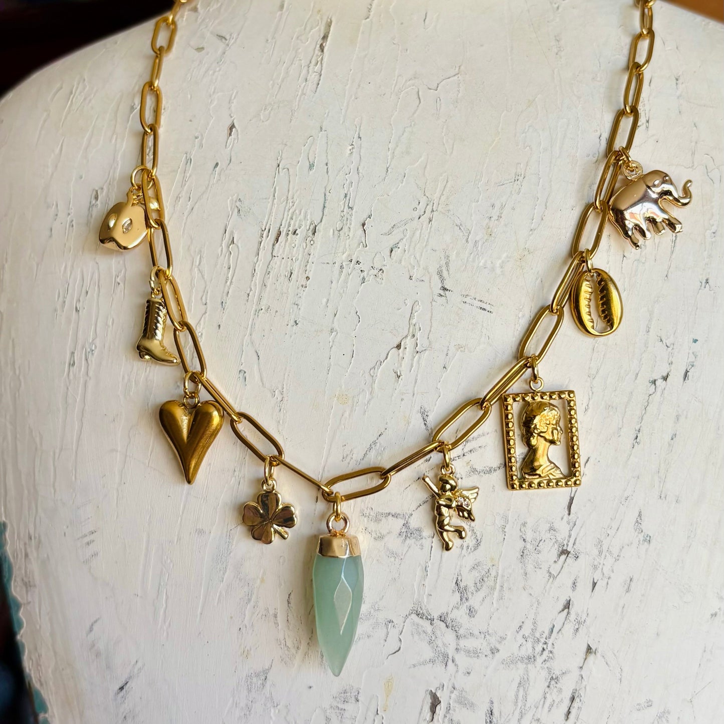Gold necklace with charms on a mannequin bust against a rustic background