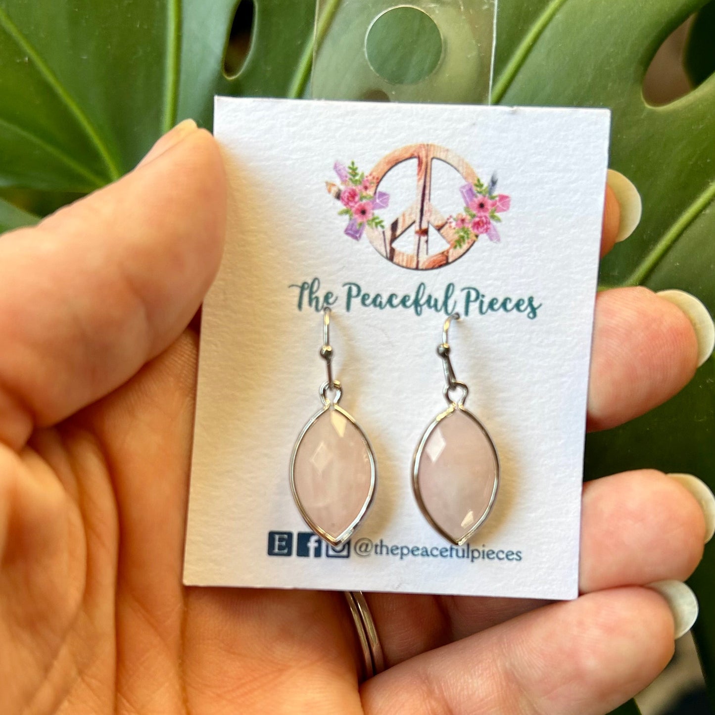 Earrings on a 'The Peaceful Pieces' card held against a green leafy background