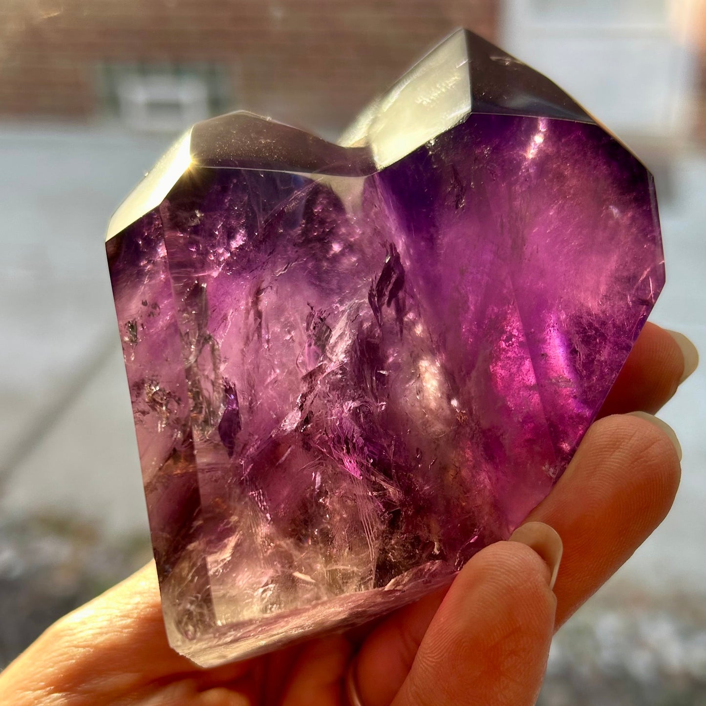 Amethyst crystal held in a hand with a blurred indoor background