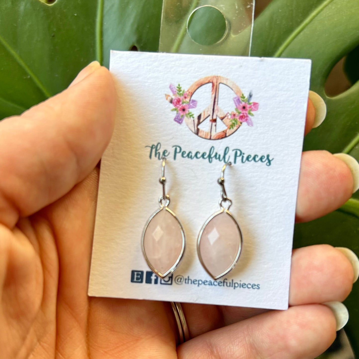 Earrings on a 'The Peaceful Pieces' card held by a hand with a green leafy background