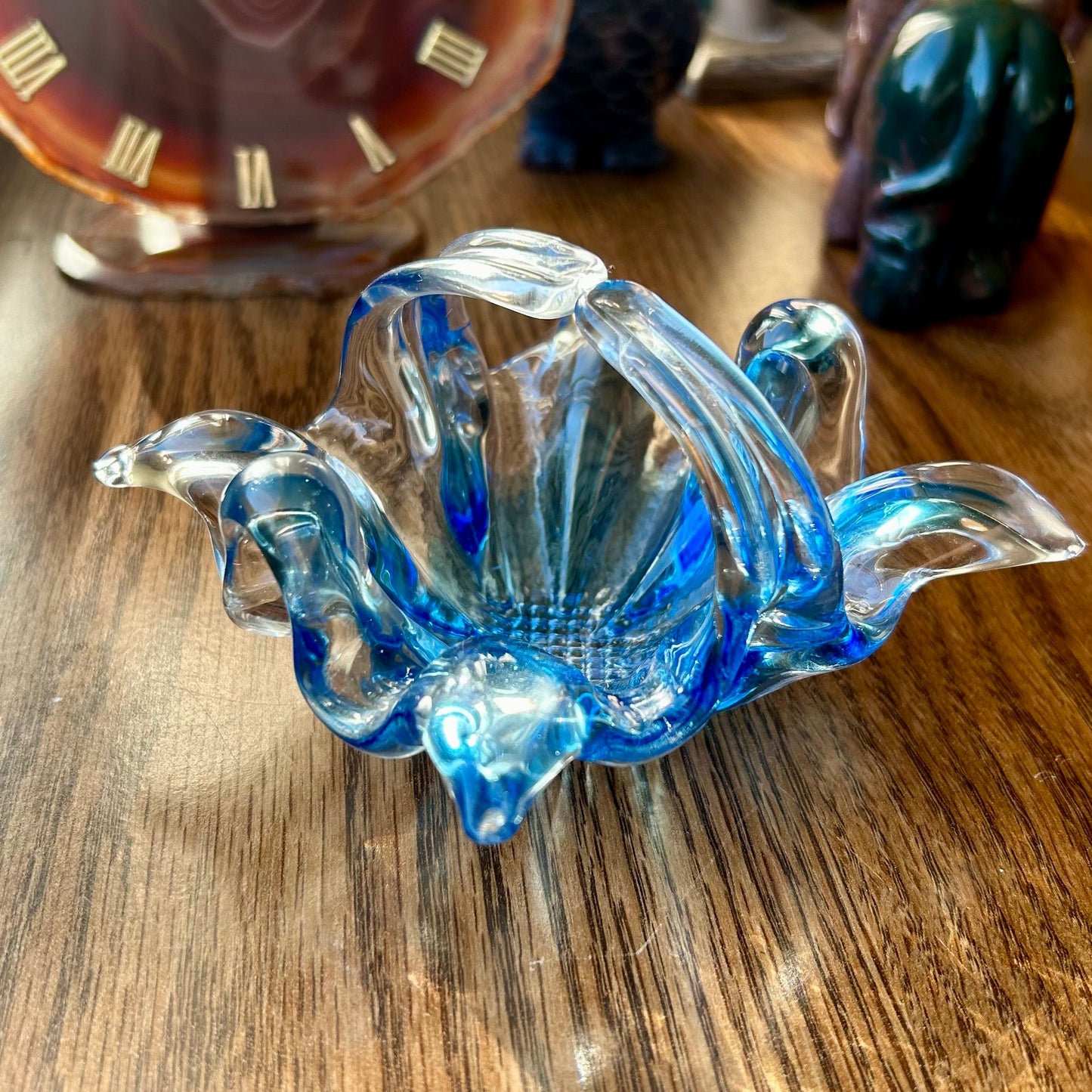 Blue glass sculpture on a wooden surface with a clock in the background