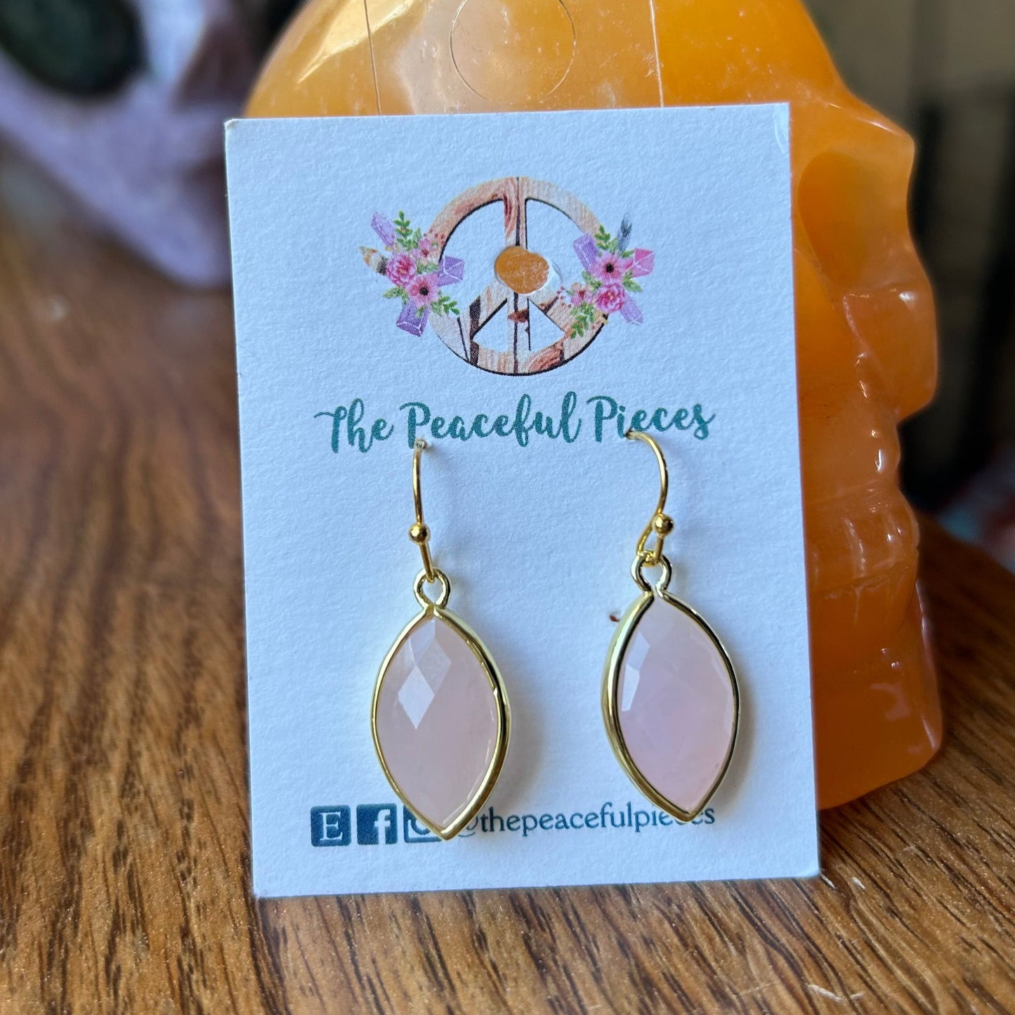 Pink teardrop earrings on a 'The Peaceful Pieces' card with a blurred background