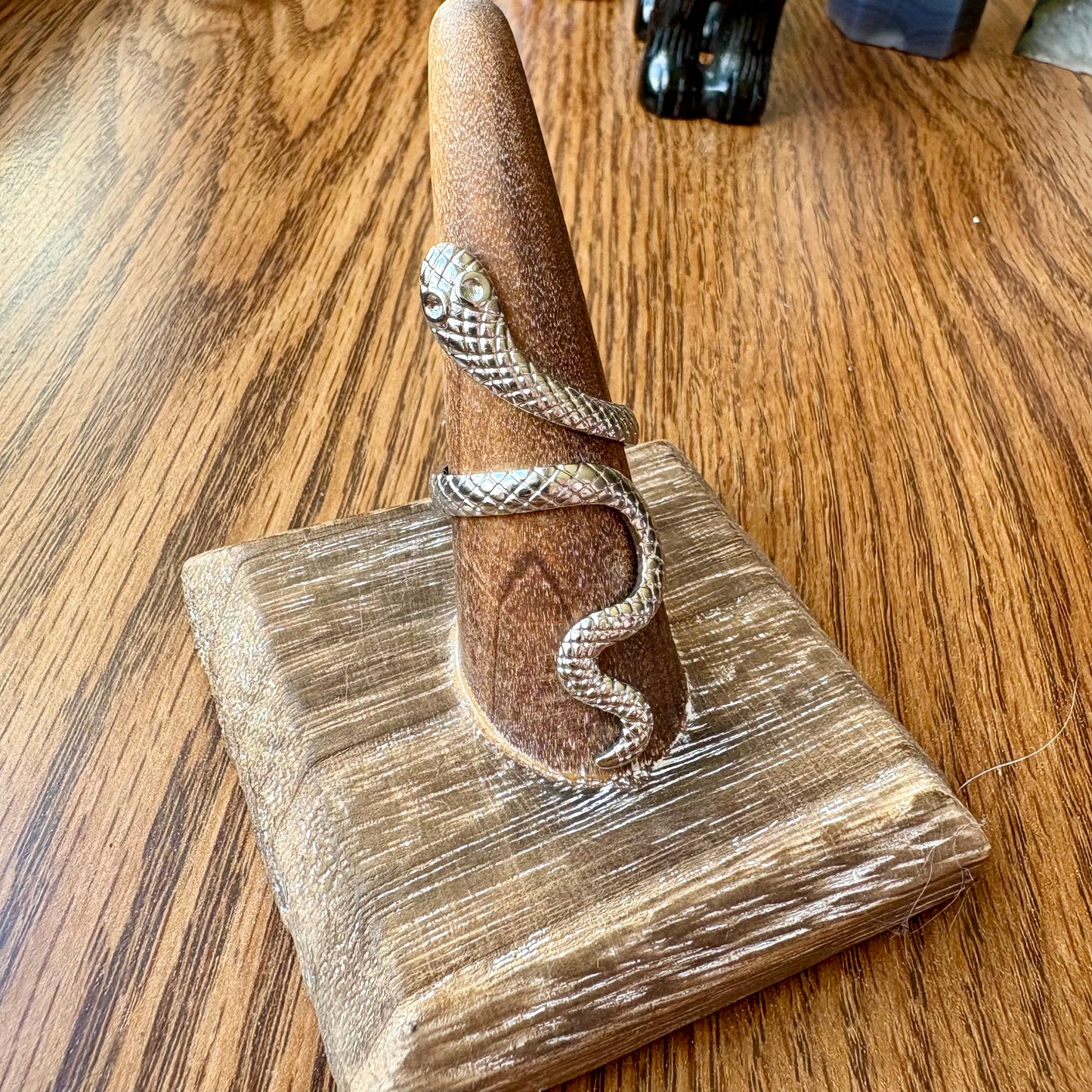 Silver ring on a wooden stand with a snake design on a wooden surface
