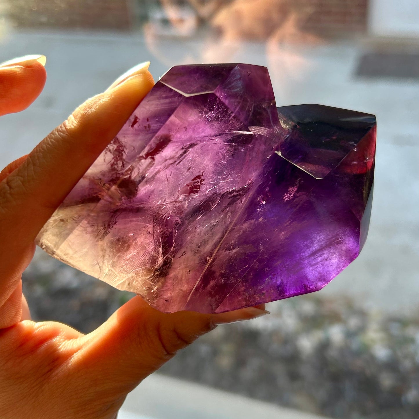 Hand holding a purple crystal in front of a window with a blurred background