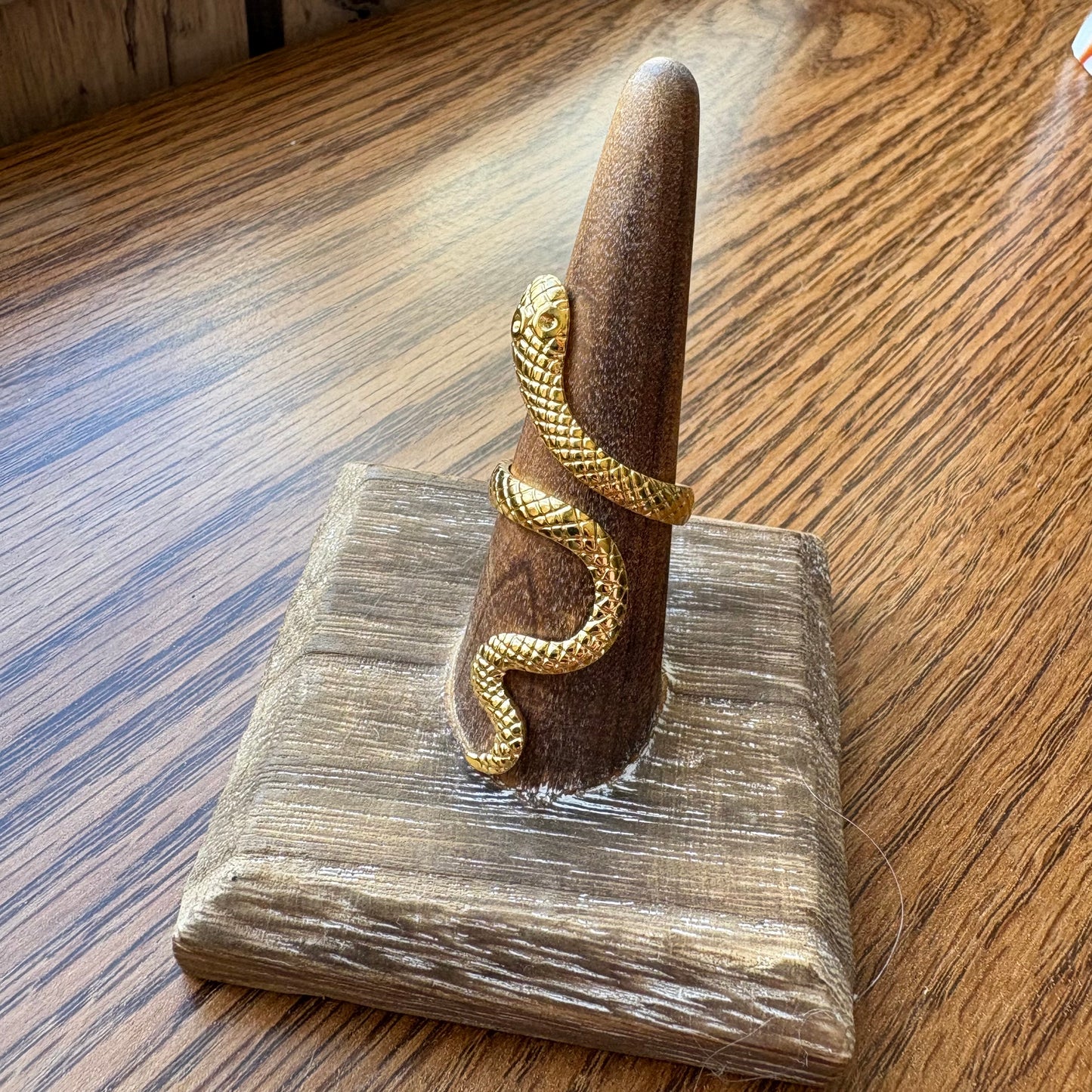 Gold snake-shaped ring on a wooden stand with a wooden floor background