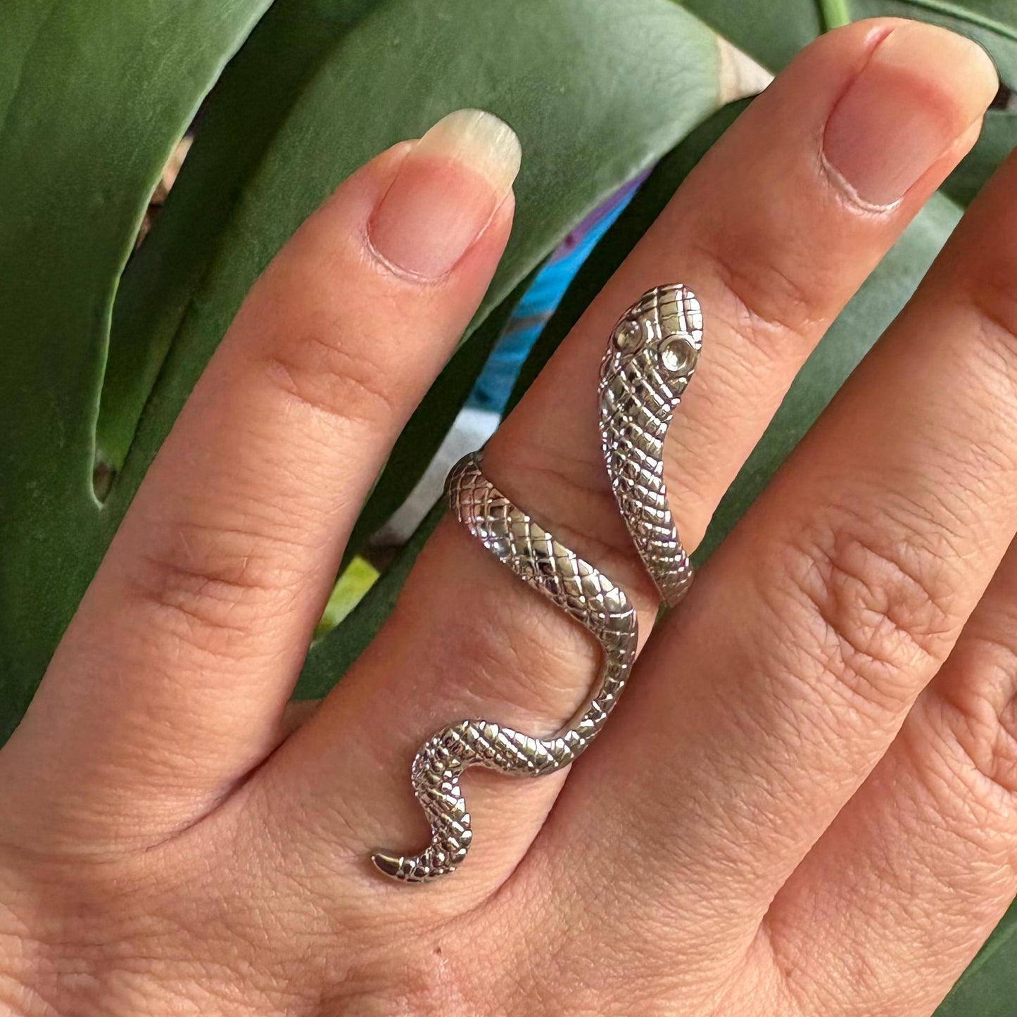 Silver snake-shaped ring on a finger with a green leafy background