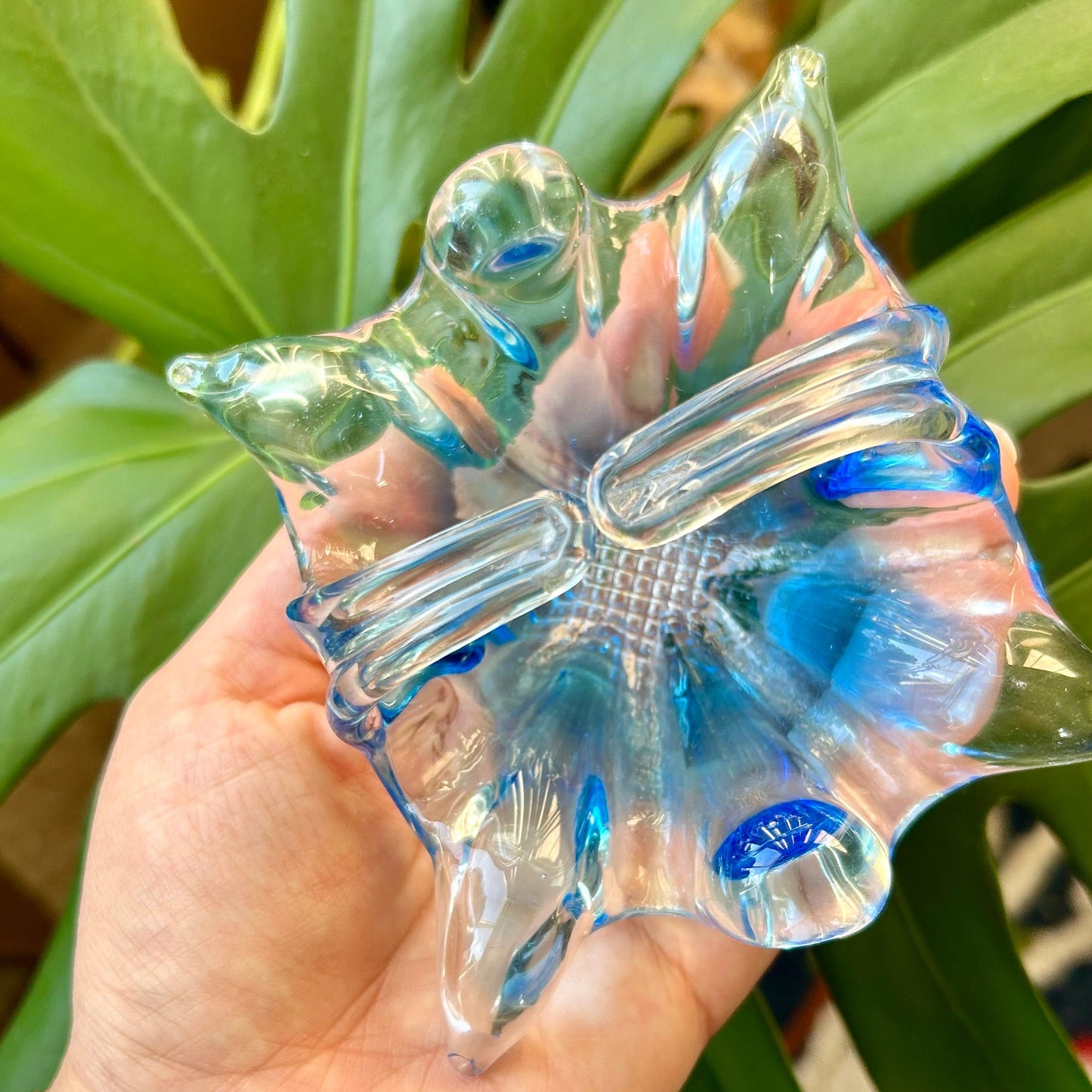 Hand holding a clear butterfly-shaped object with a blurred green plant background