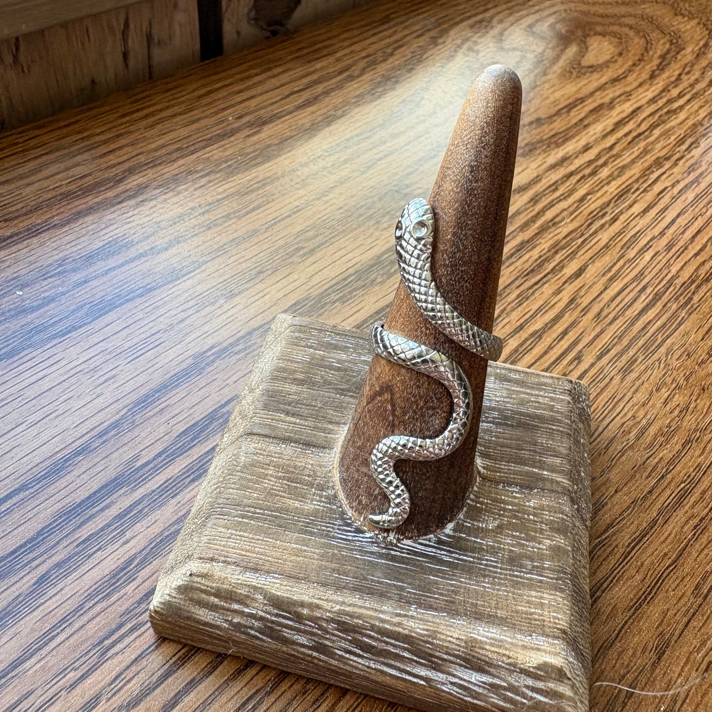 Silver snake-shaped ring on a wooden stand with a wooden background