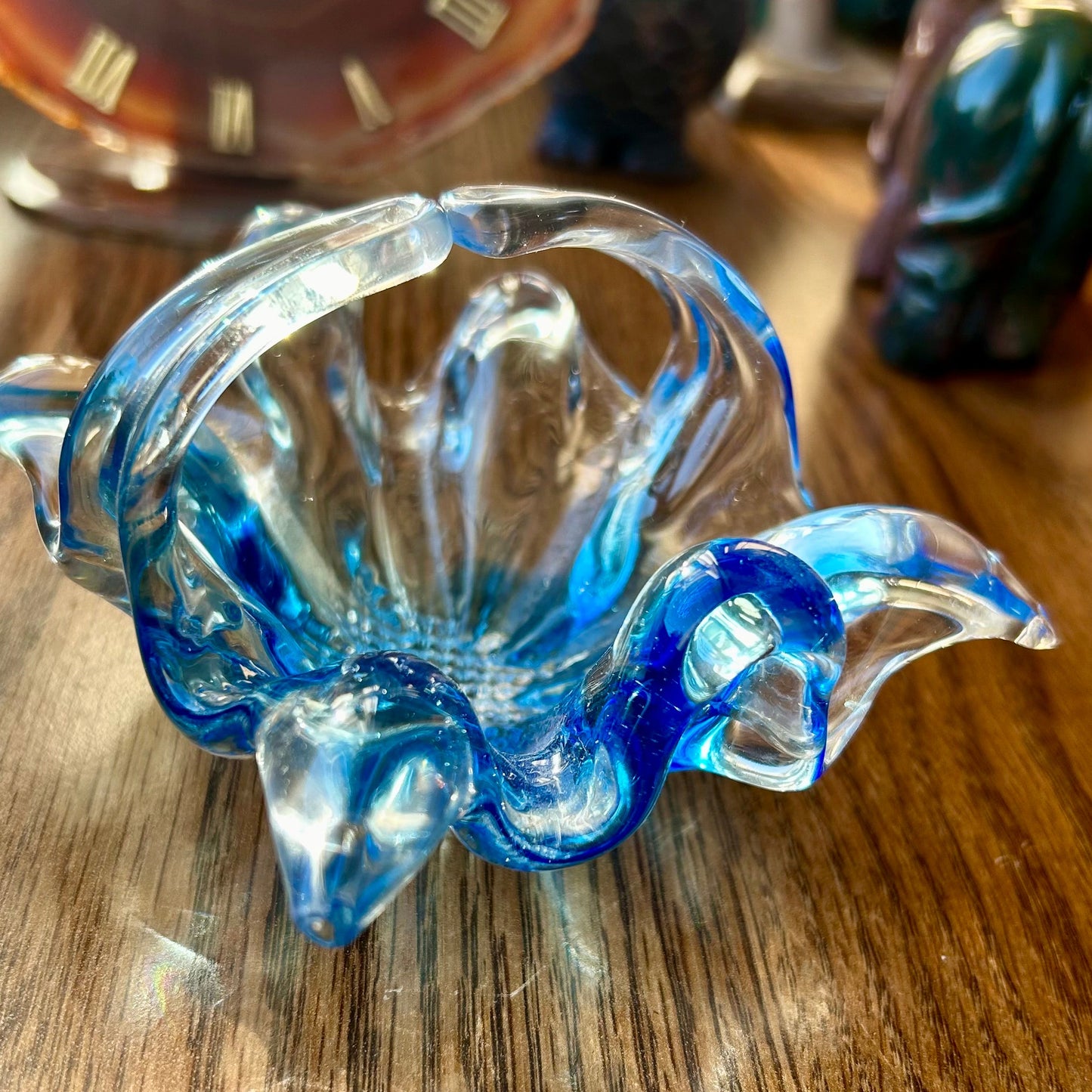 Blue glass sculpture on a wooden surface with a clock in the background