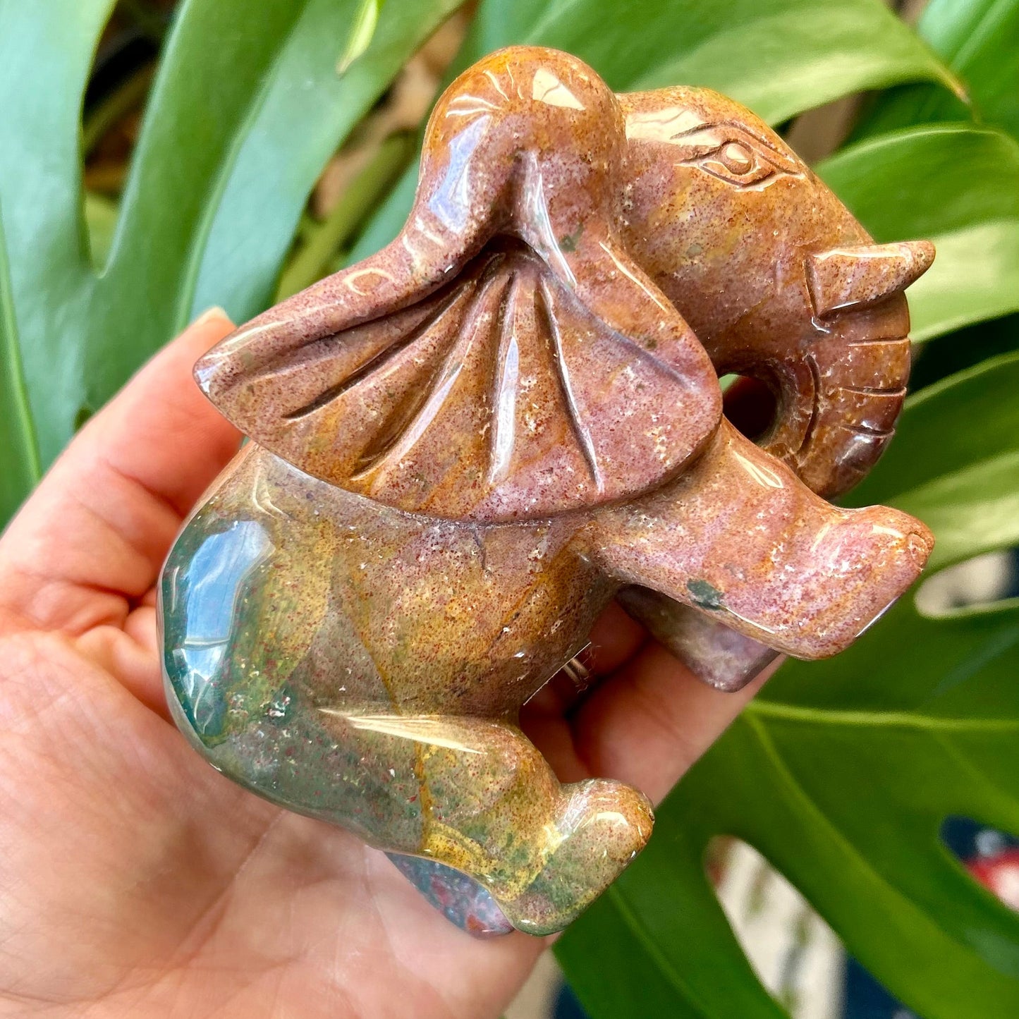 Hand holding a small brown stone sculpture against a green leafy background