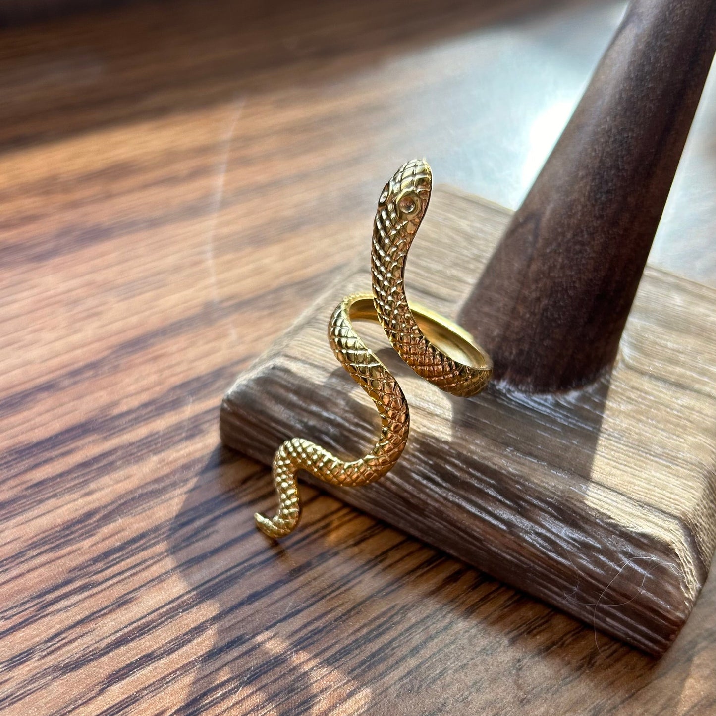 Gold snake-shaped ring on a wooden stand