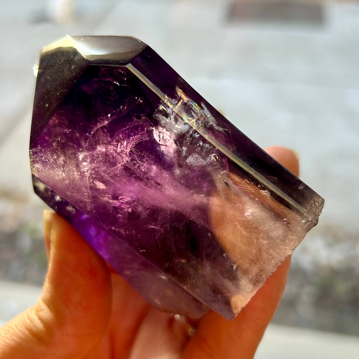 Amethyst crystal held in a hand with a blurred background