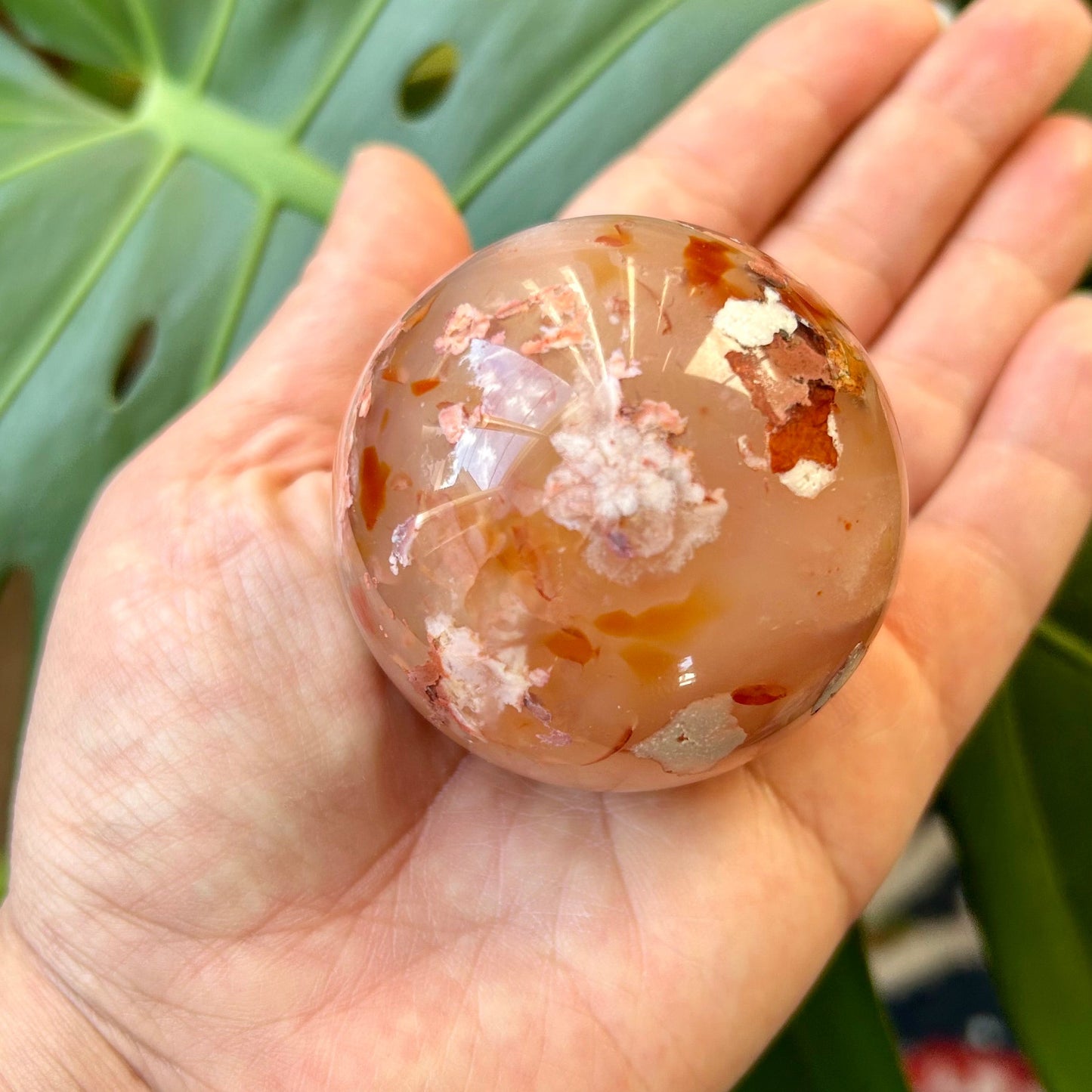 Hand holding a crystal ball with a textured surface against a green leaf background
