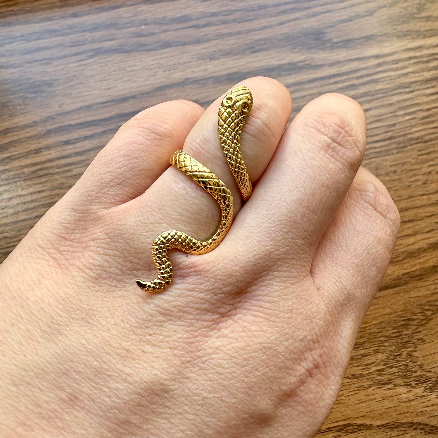 Gold snake-shaped ring on a person's finger with a wooden background