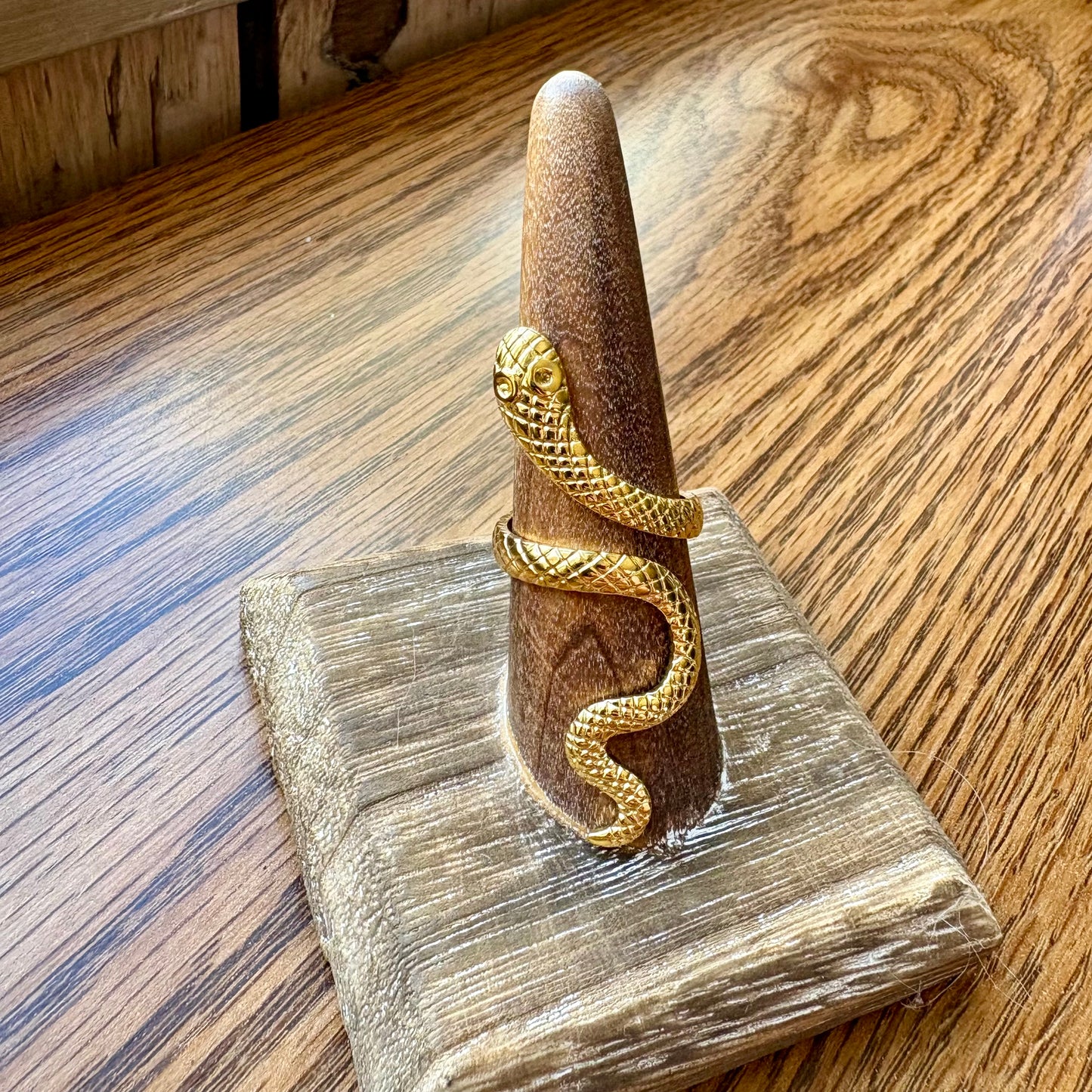 Gold snake-shaped ring on a wooden stand with a wooden background