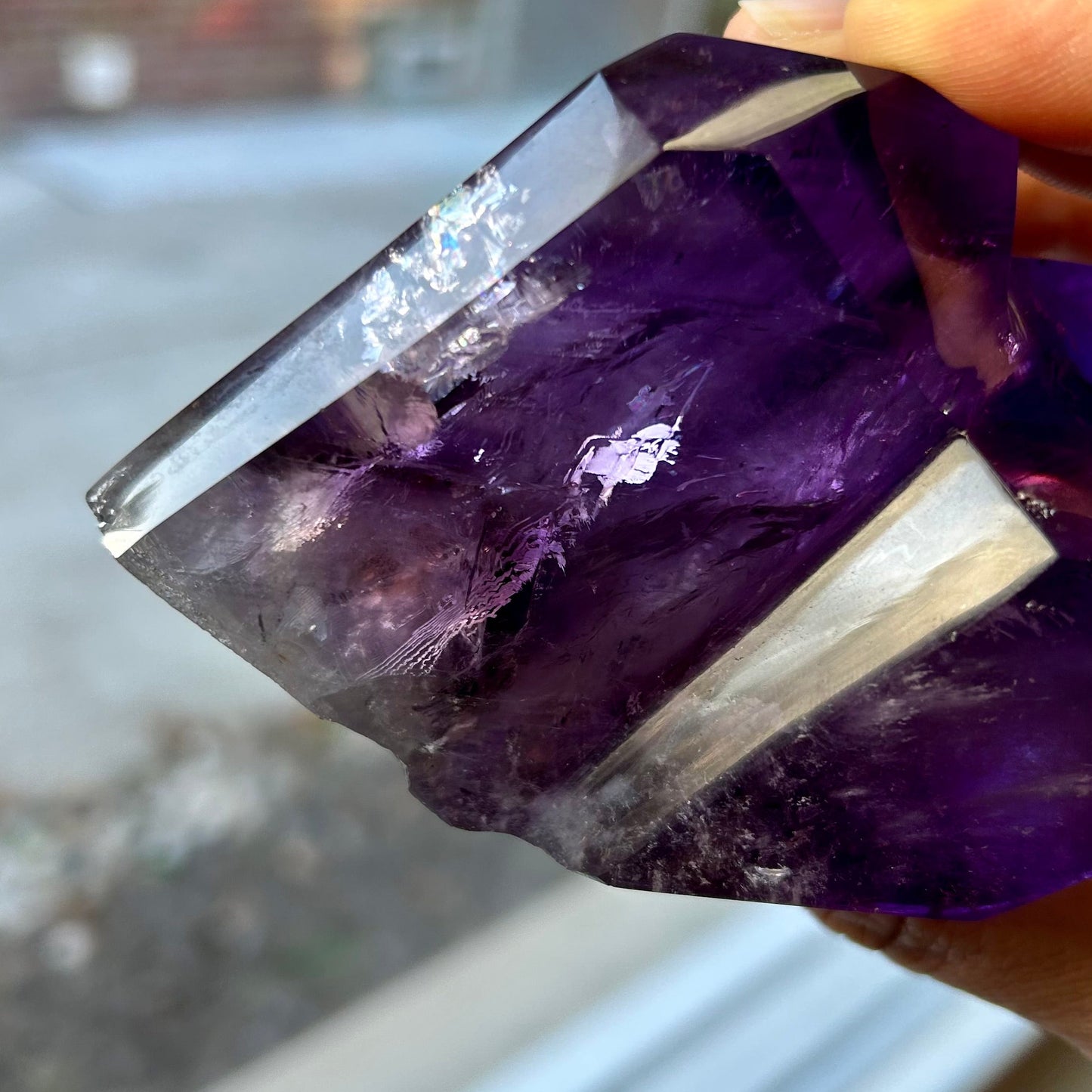 Amethyst crystal held by a hand with a blurred outdoor background