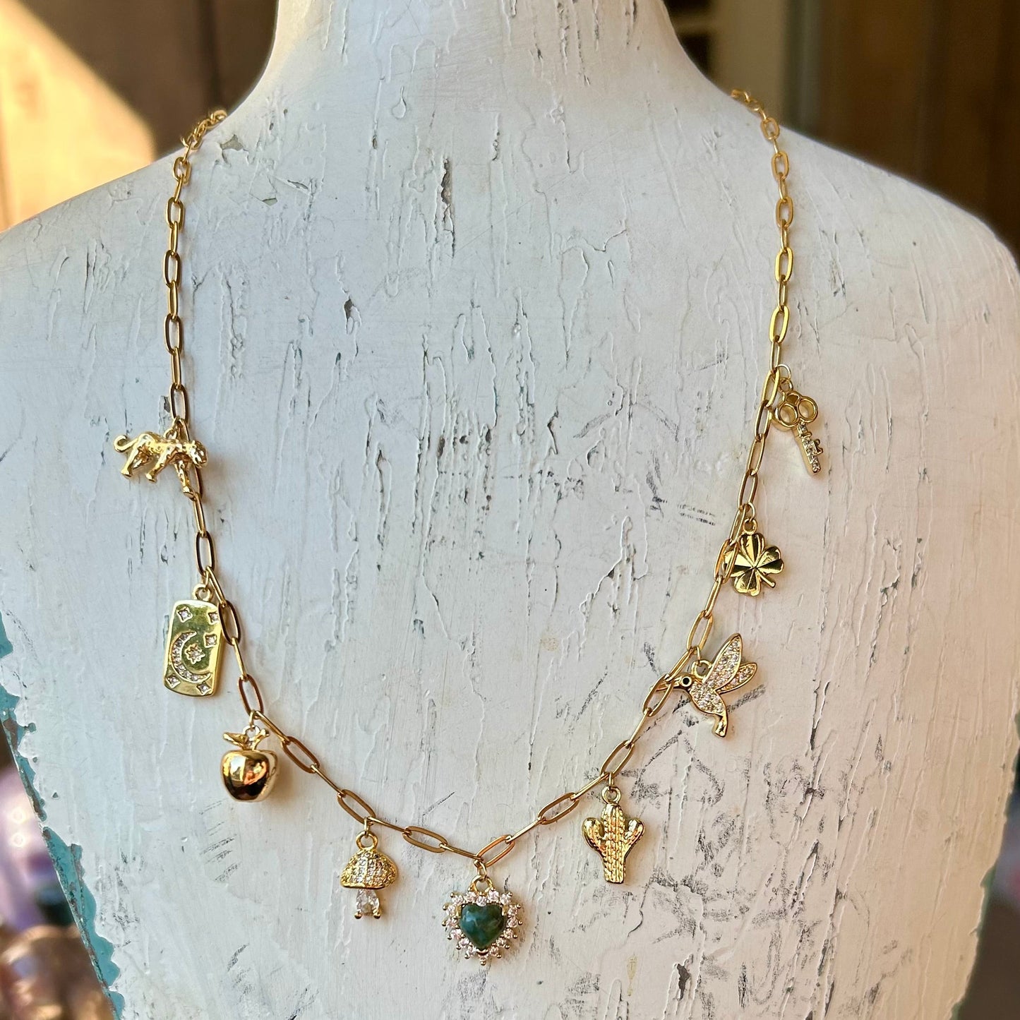 Gold necklace with charms on a white distressed wooden stand.