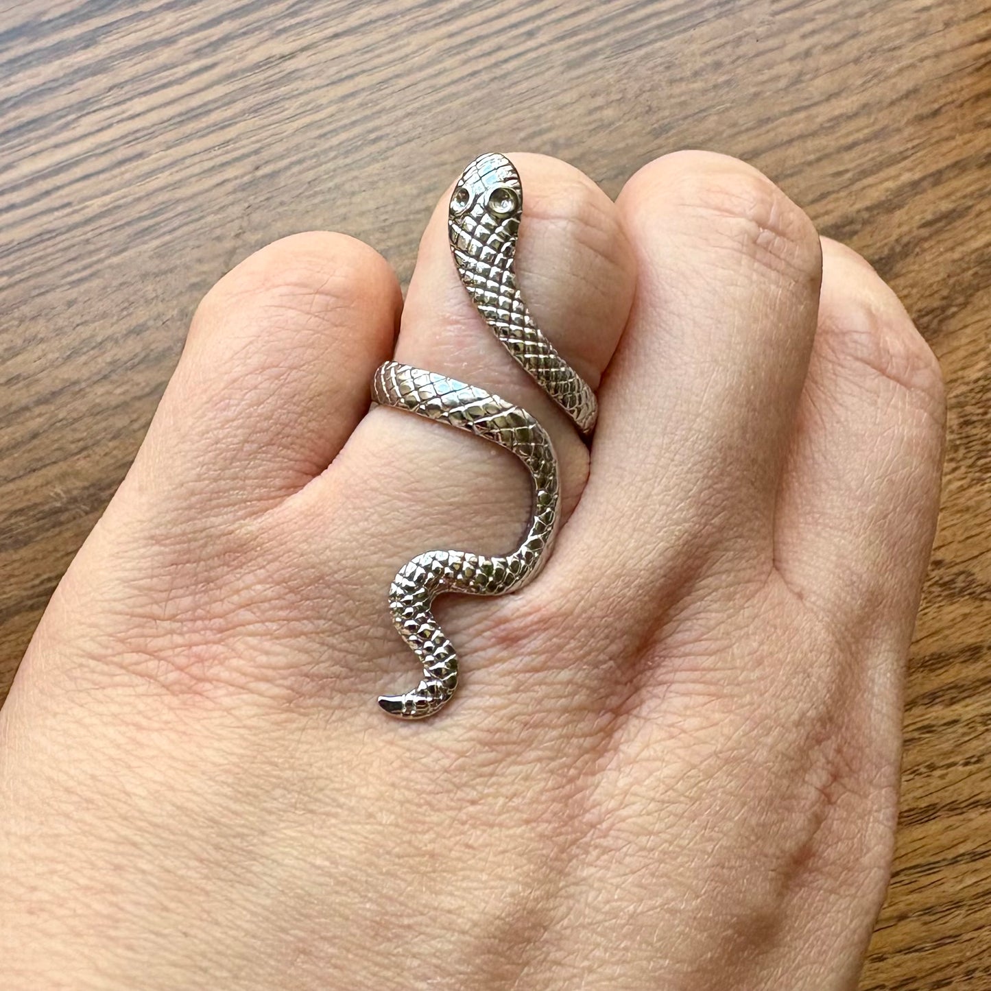 Silver snake-shaped ring on a finger with a wooden background