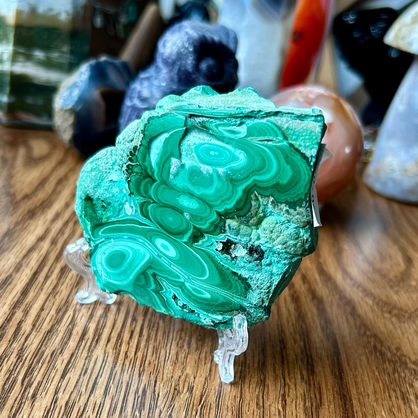Green malachite crystal on a wooden surface with other crystals in the background