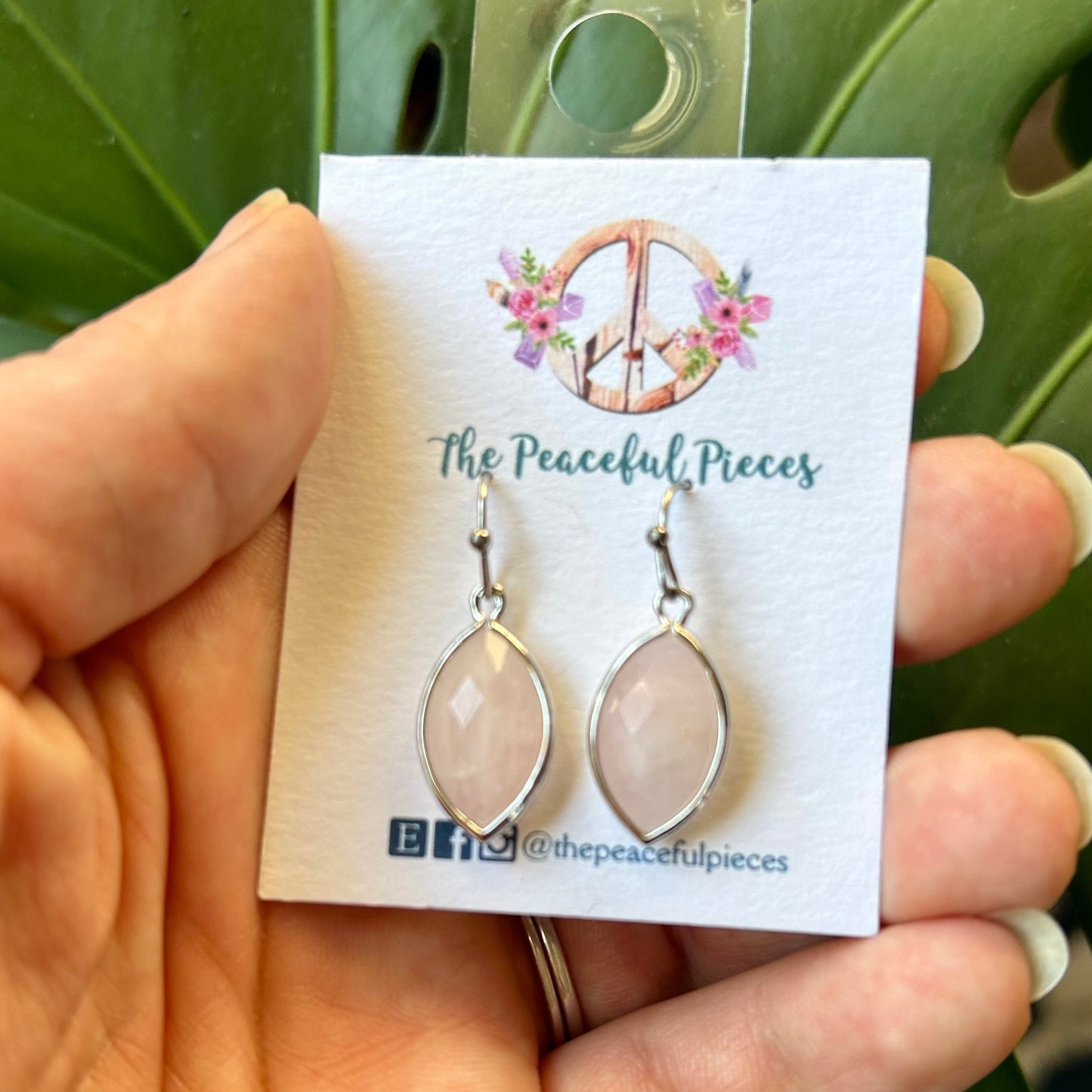 Earrings on a 'The Peaceful Pieces' card held in a hand with a green leafy background