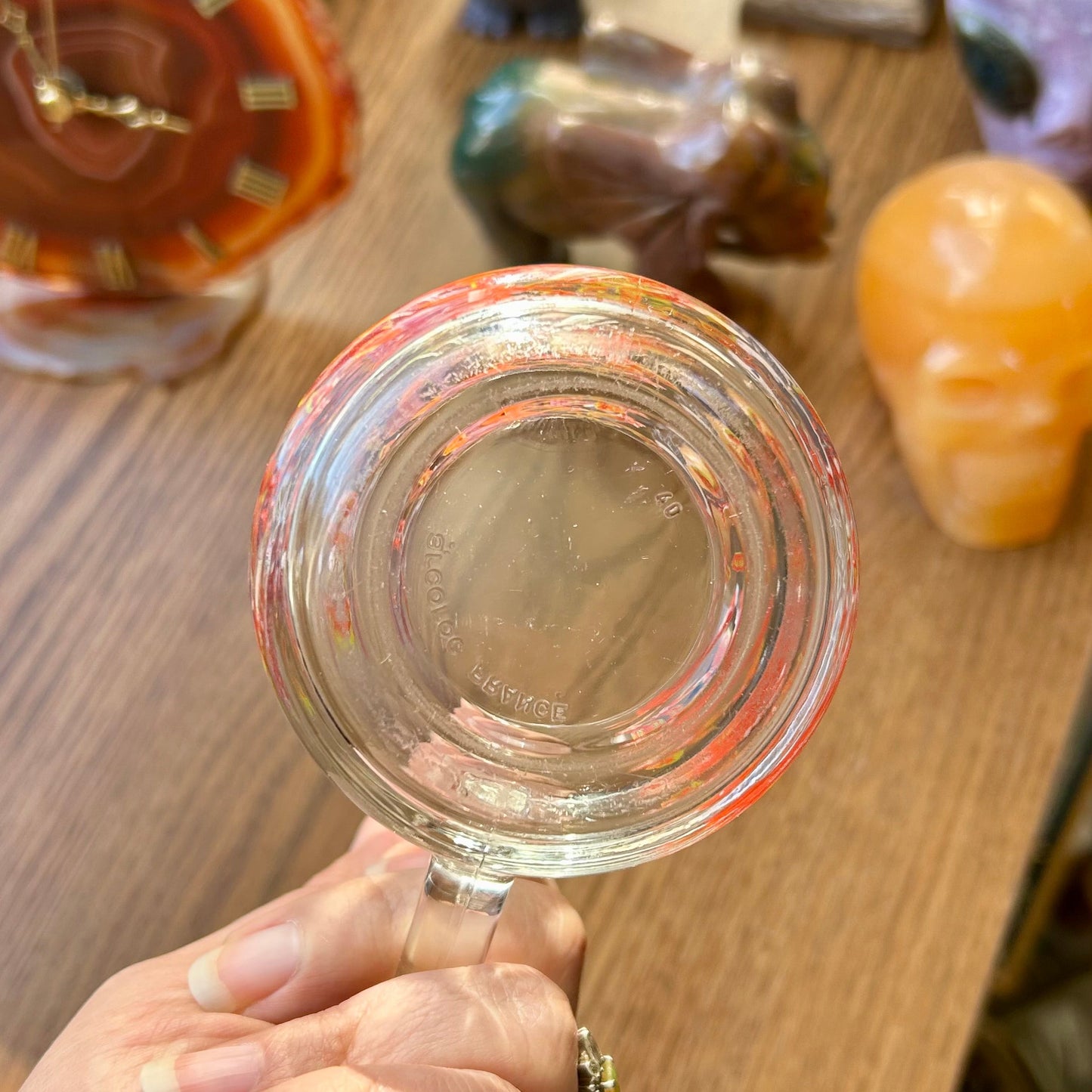 Hand holding a clear glass magnifying glass over a wooden surface with various objects.