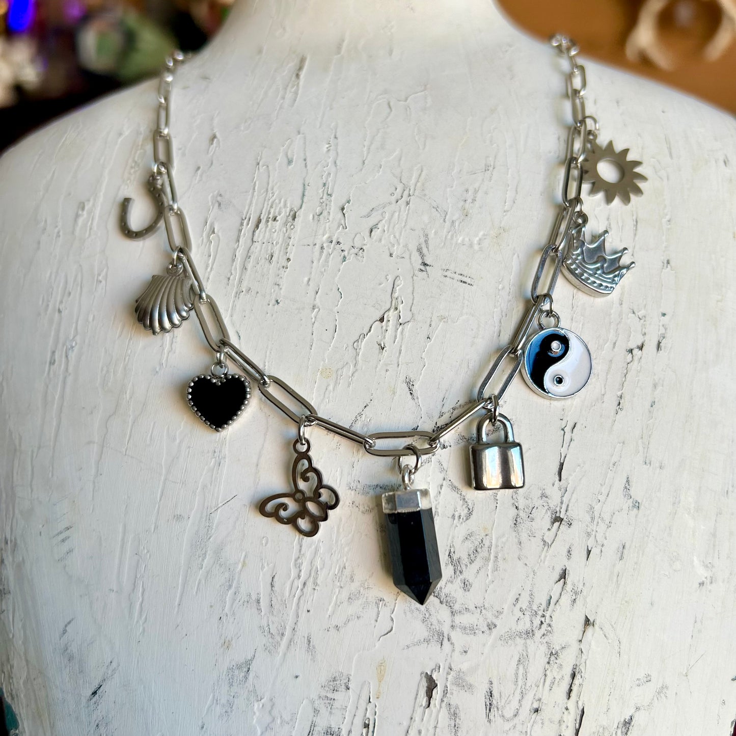 Necklace with various charms on a mannequin against a textured white background