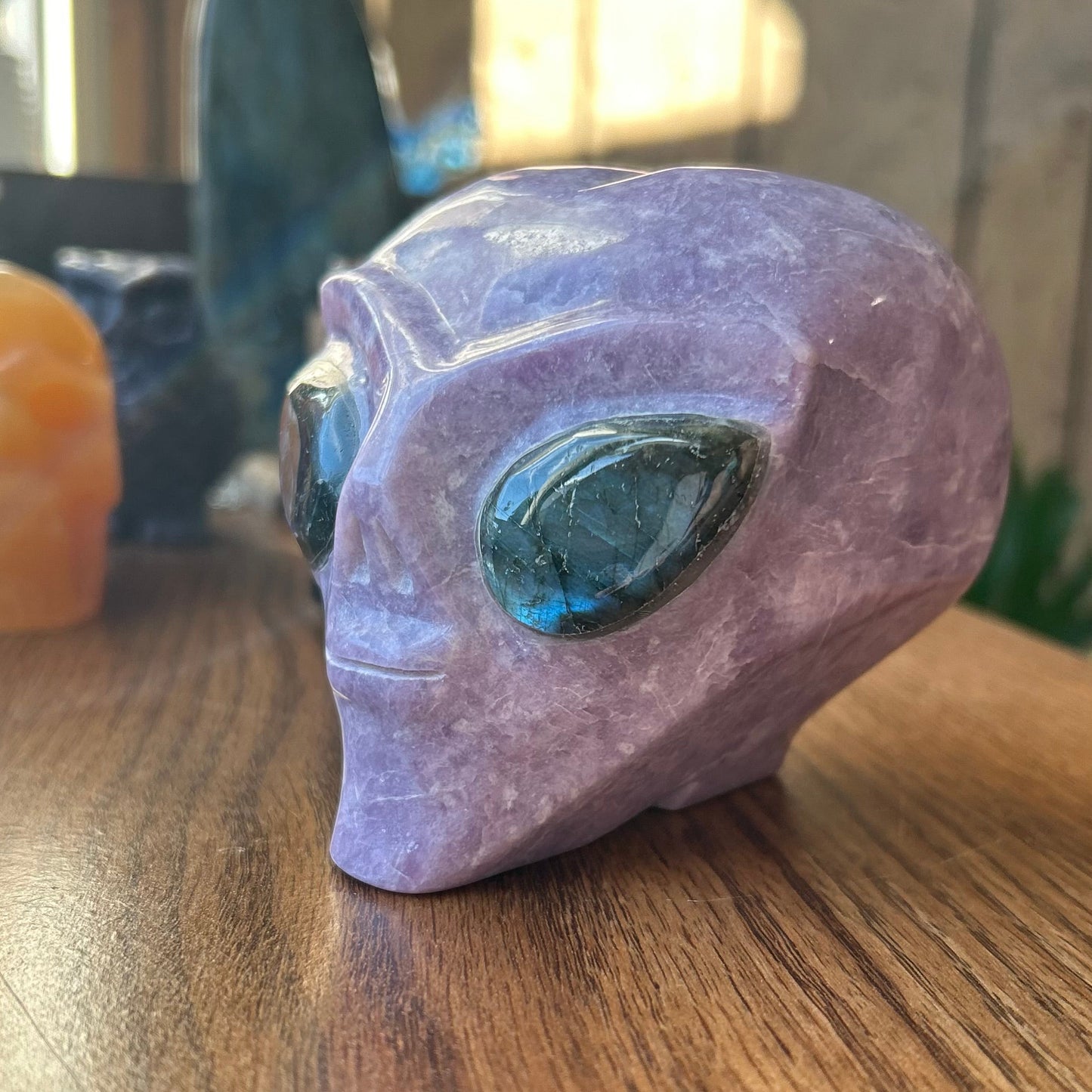 Pink alien head sculpture with a green gemstone on a wooden surface