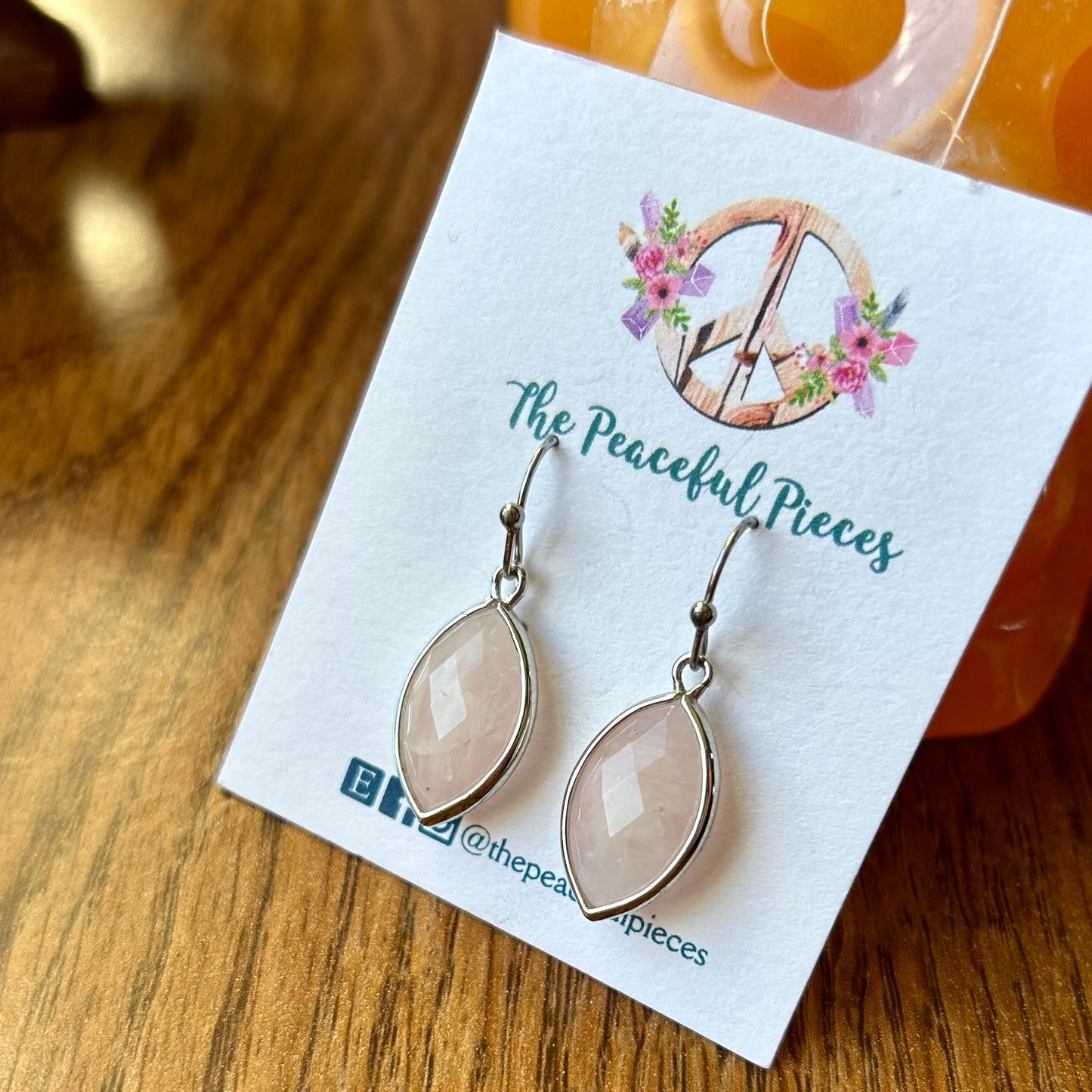 Pair of earrings on a 'The Peaceful Pieces' branded card on a wooden surface.