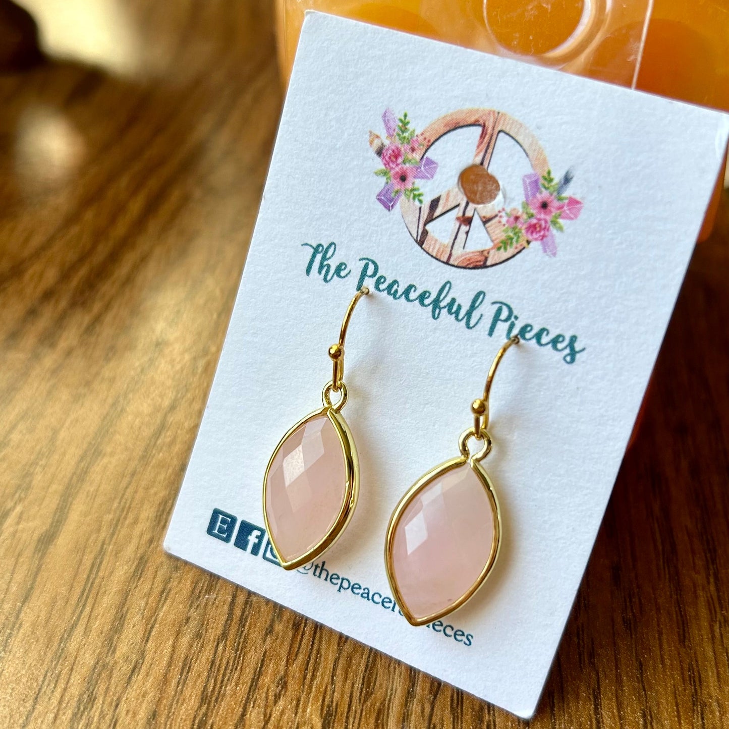 Pair of earrings on a 'The Peaceful Pieces' branded card on a wooden surface.