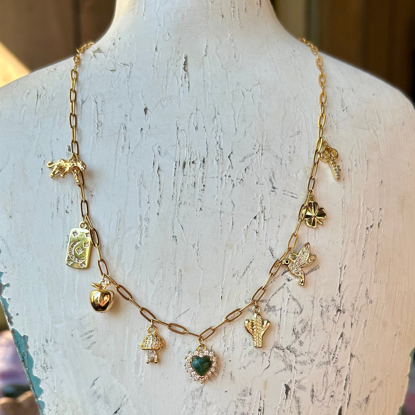 Gold necklace with various charms on a rustic wooden stand.