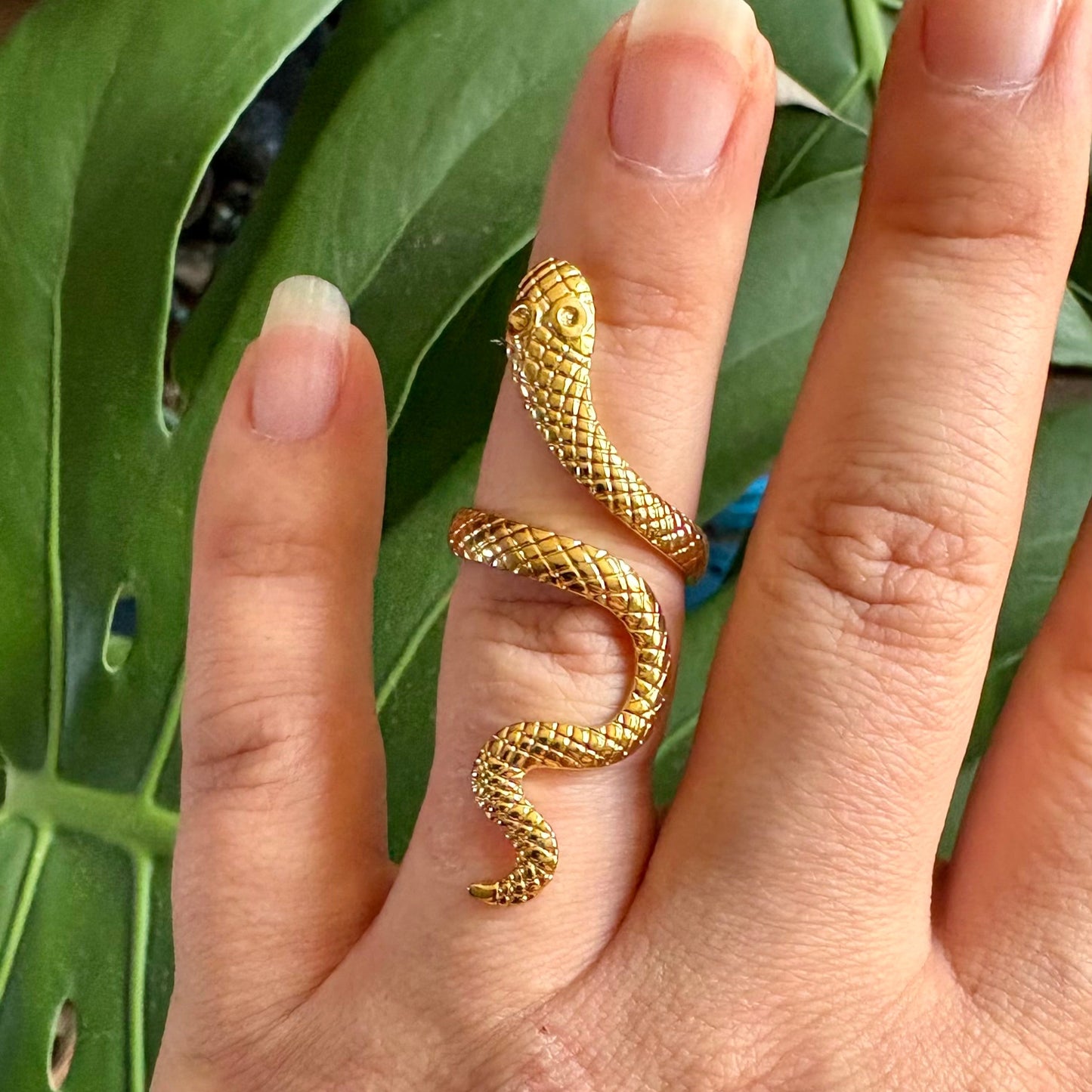 Gold snake-shaped ring on a finger with a green leafy background
