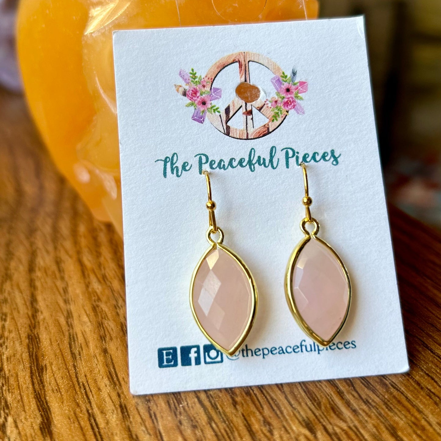 Pink teardrop earrings on a 'The Peaceful Pieces' card with a blurred background