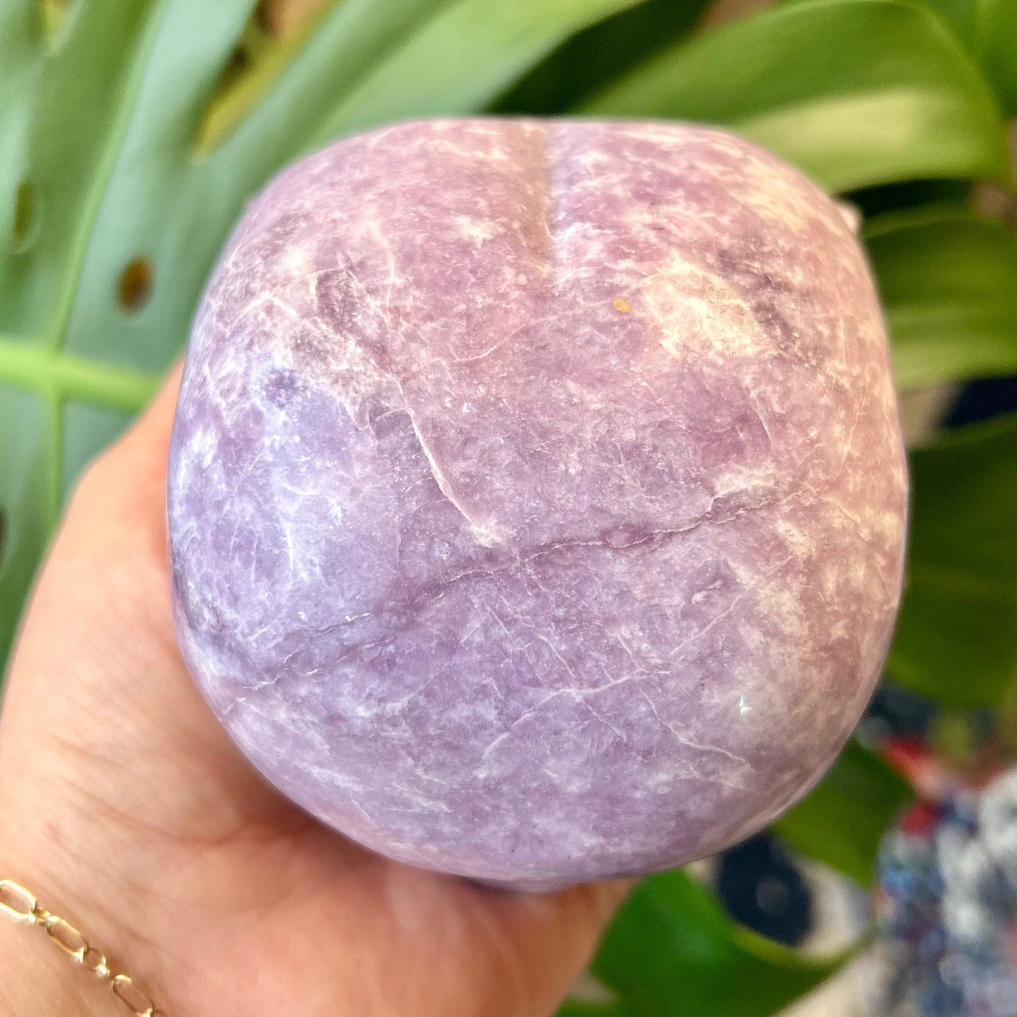 Purple bath bomb held in a hand with green leaves in the background