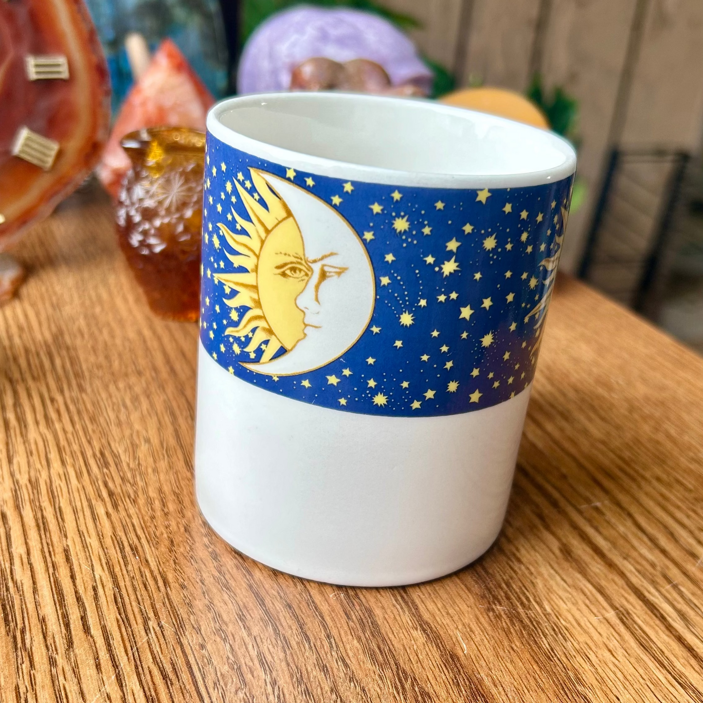 White mug with blue sleeve featuring celestial design on a wooden surface