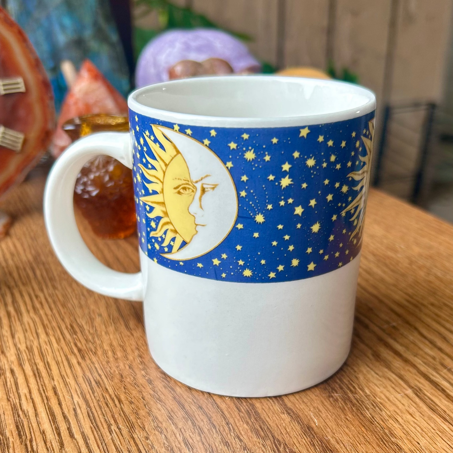 White mug with blue design featuring a sun and stars on a wooden surface.