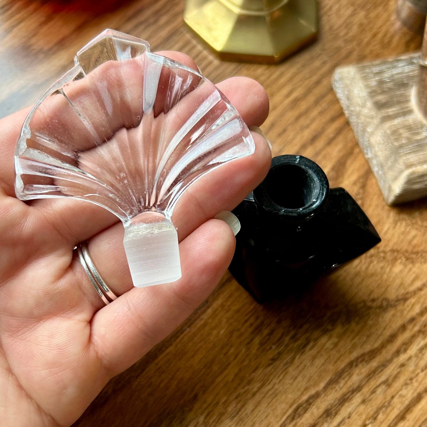 Hand holding a clear glass shell-shaped object on a wooden surface