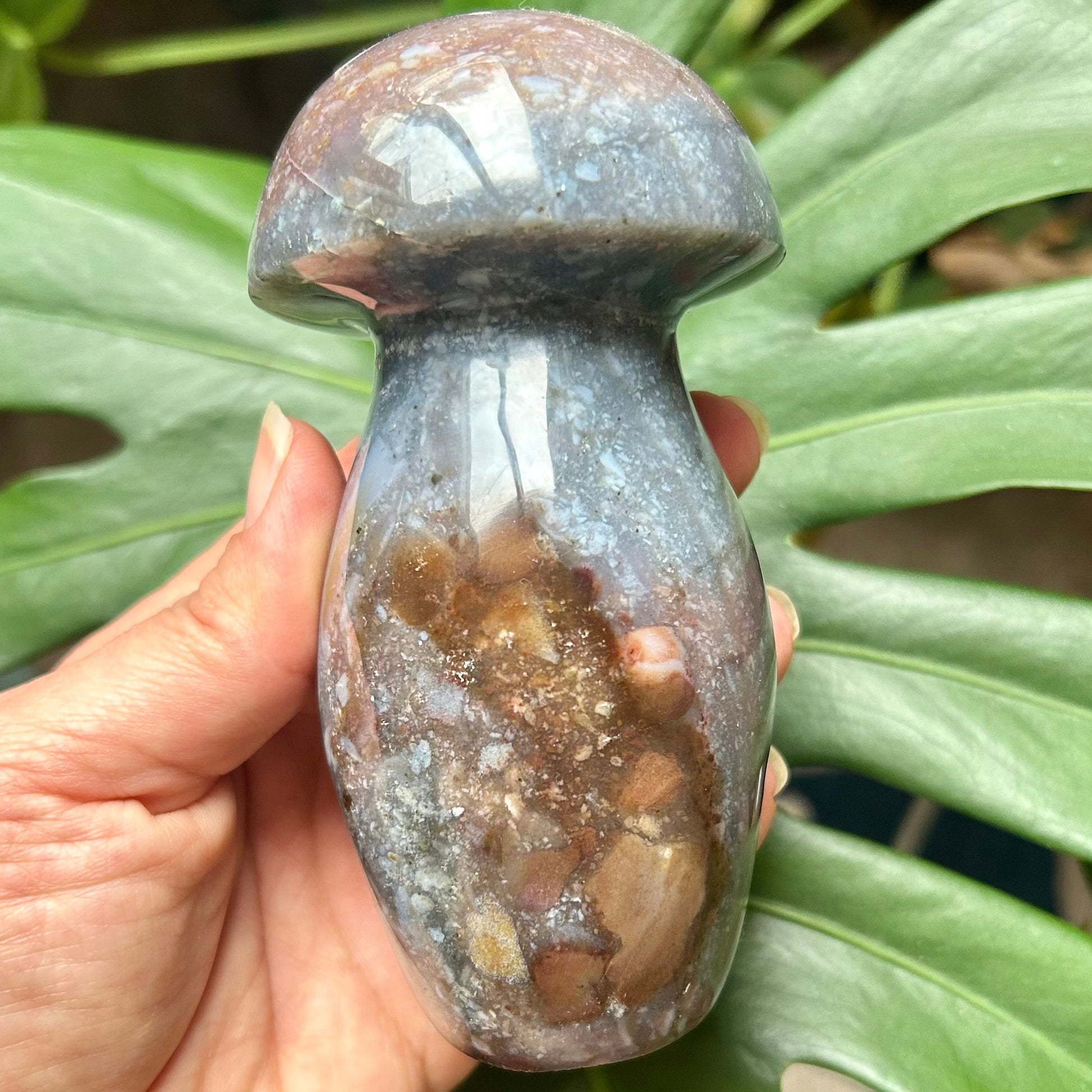 Hand holding a textured stone object with green leaves in the background