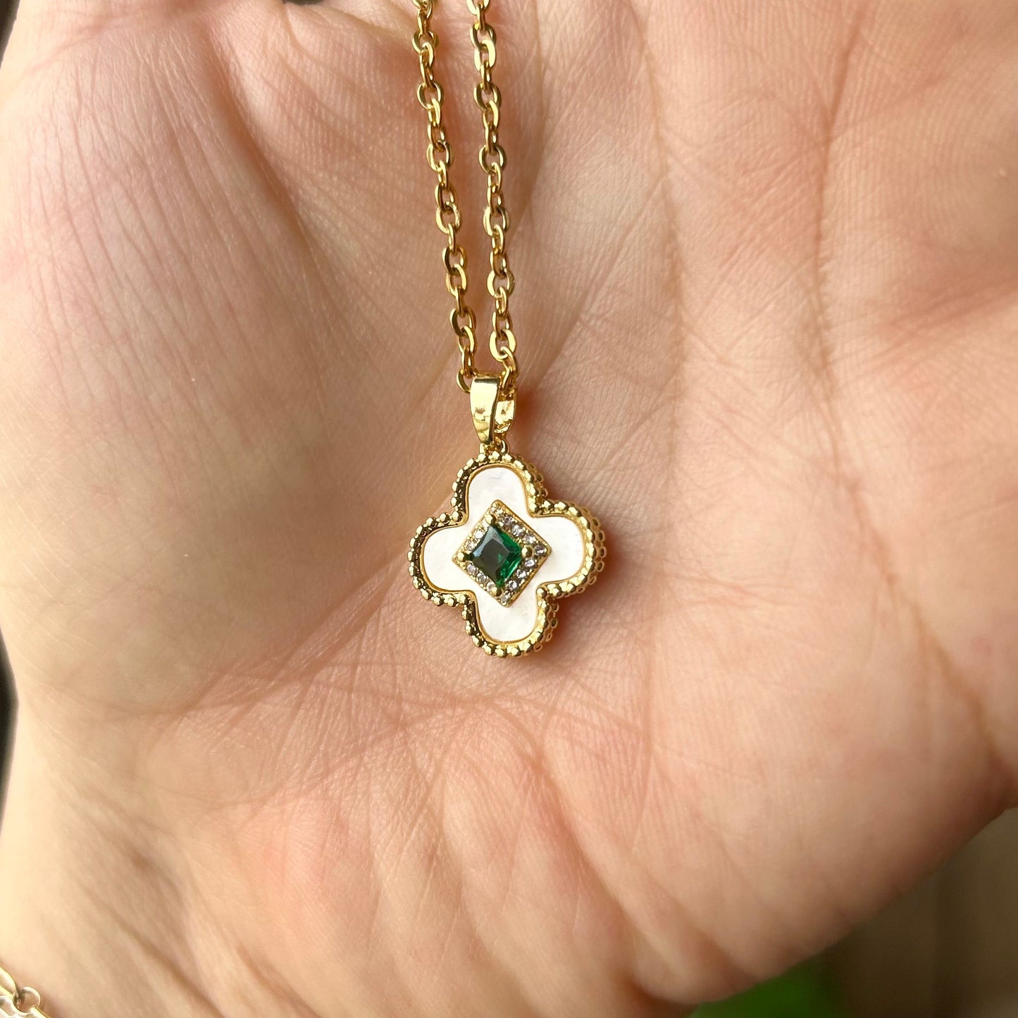 Gold necklace with a clover-shaped pendant held in a hand.