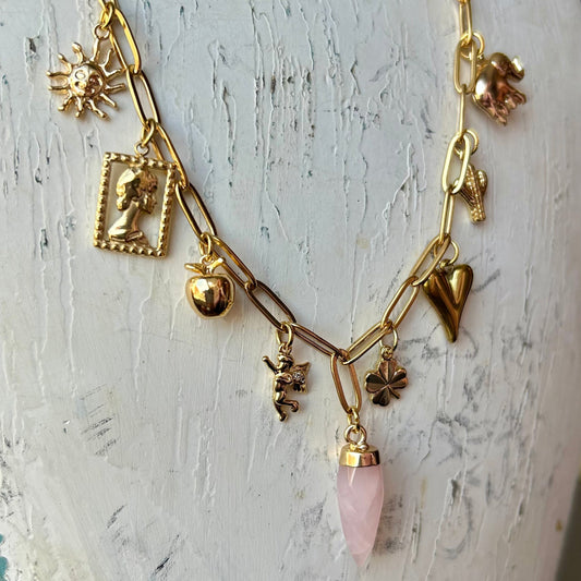 Gold necklace with various charms and a pink pendant on a white mannequin.