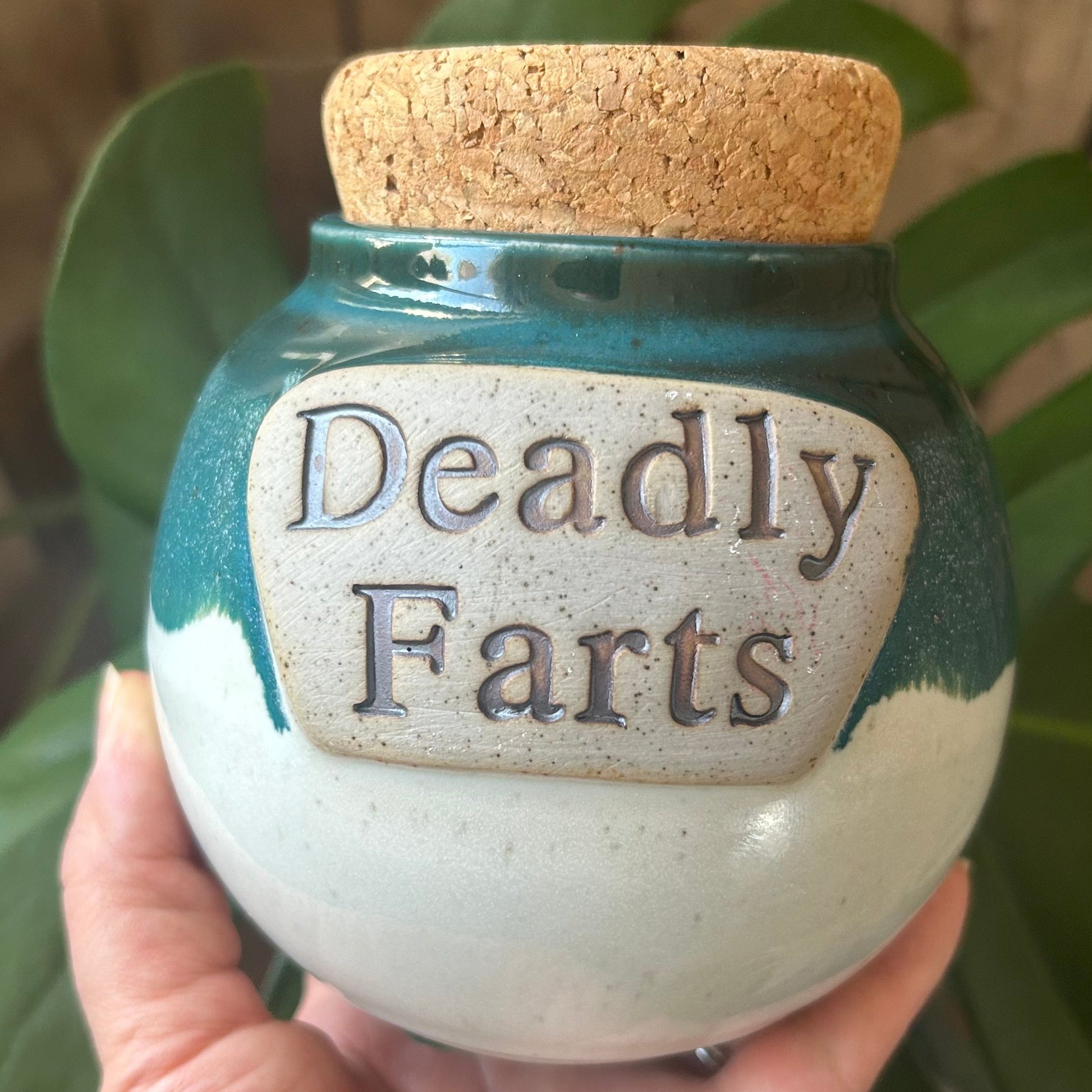Jar labeled 'Deadly Farts' held by a hand with a wooden background