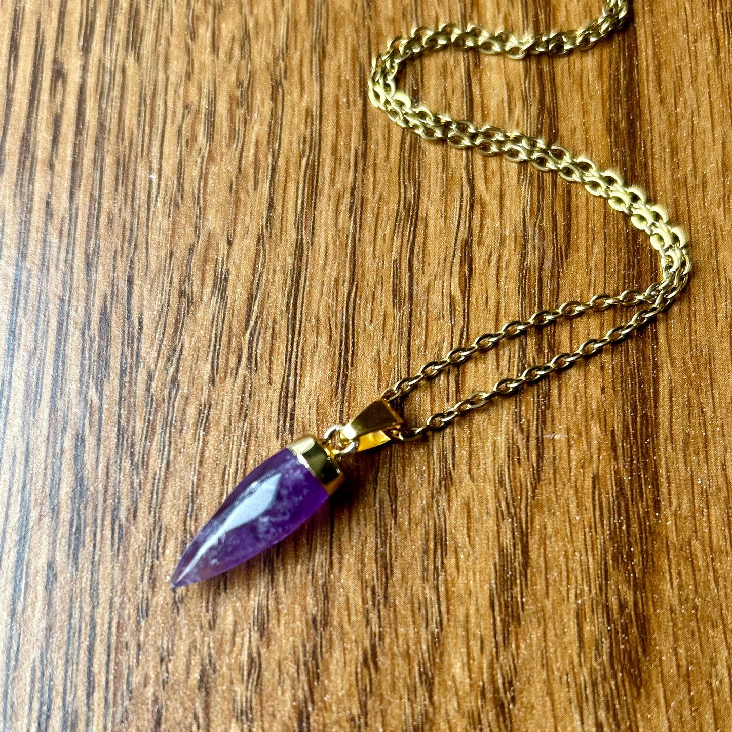Gold necklace with a purple pendant on a wooden surface