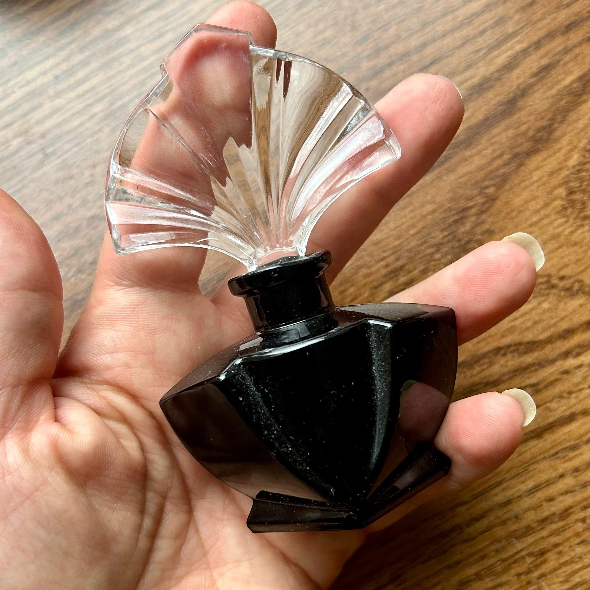 Hand holding a black and clear glass perfume bottle on a wooden surface