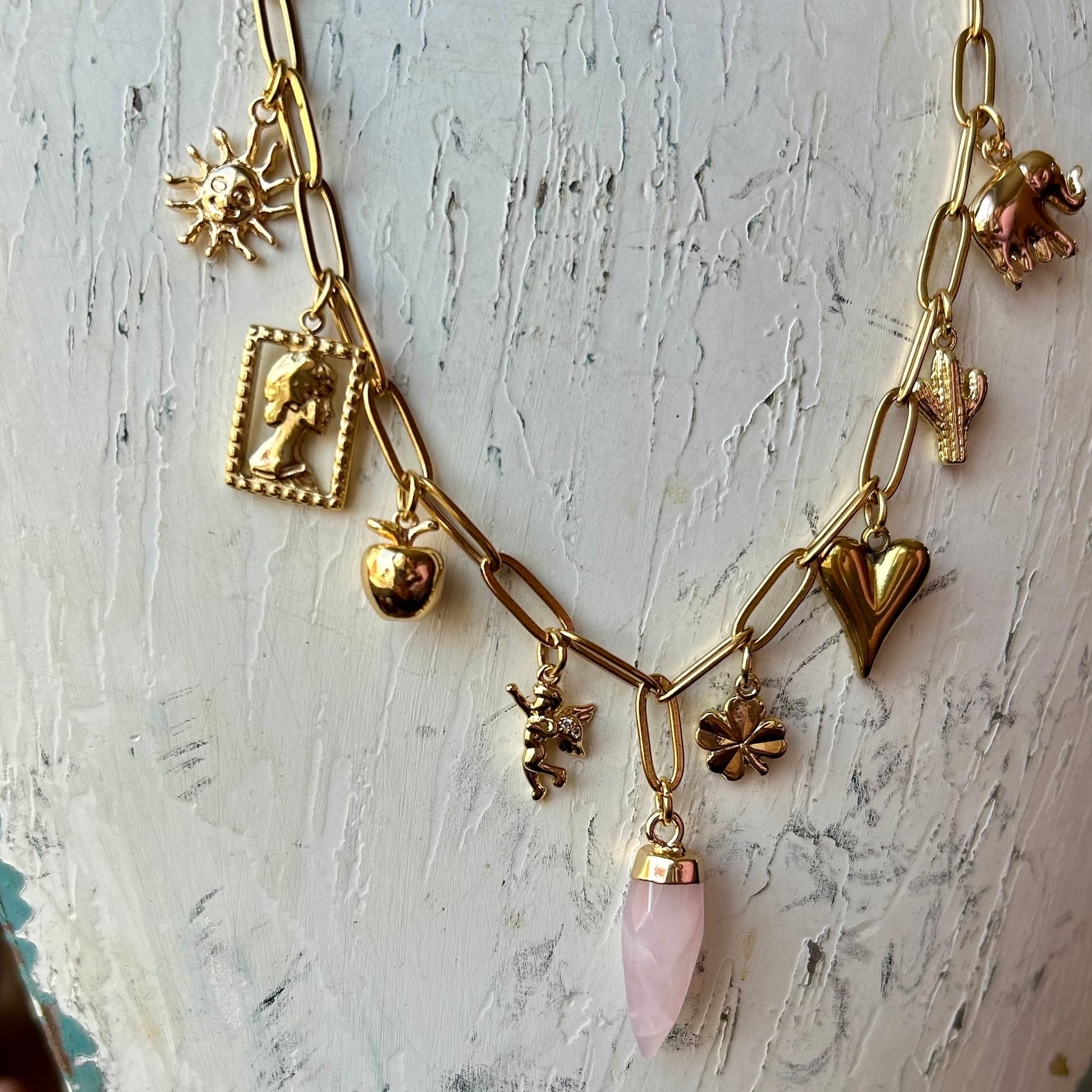 Necklace with gold chain and various charms on a textured white surface