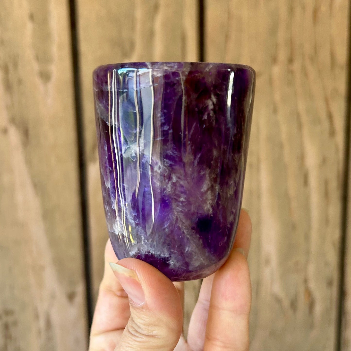 Hand holding a purple crystal cup against a wooden background