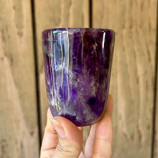 Hand holding a purple crystal cup against a wooden background