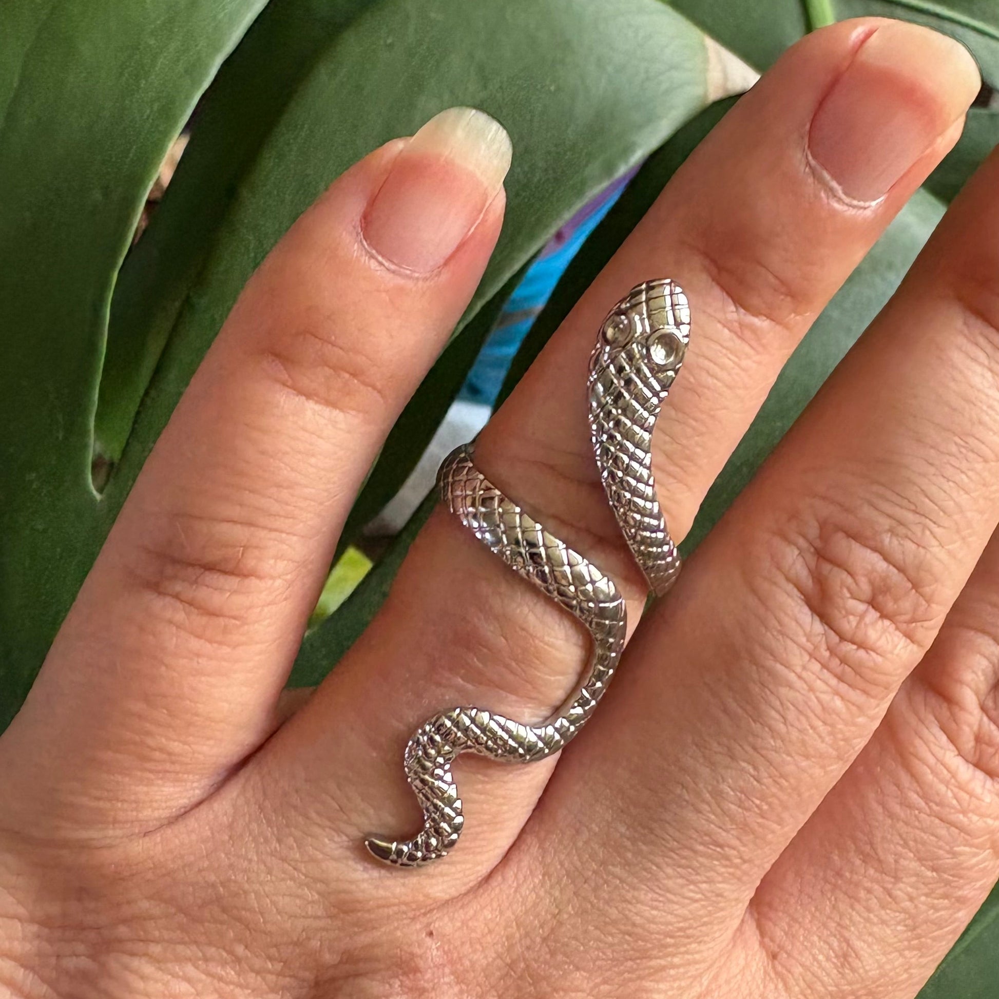 Silver snake-shaped ring on a finger with a green leafy background